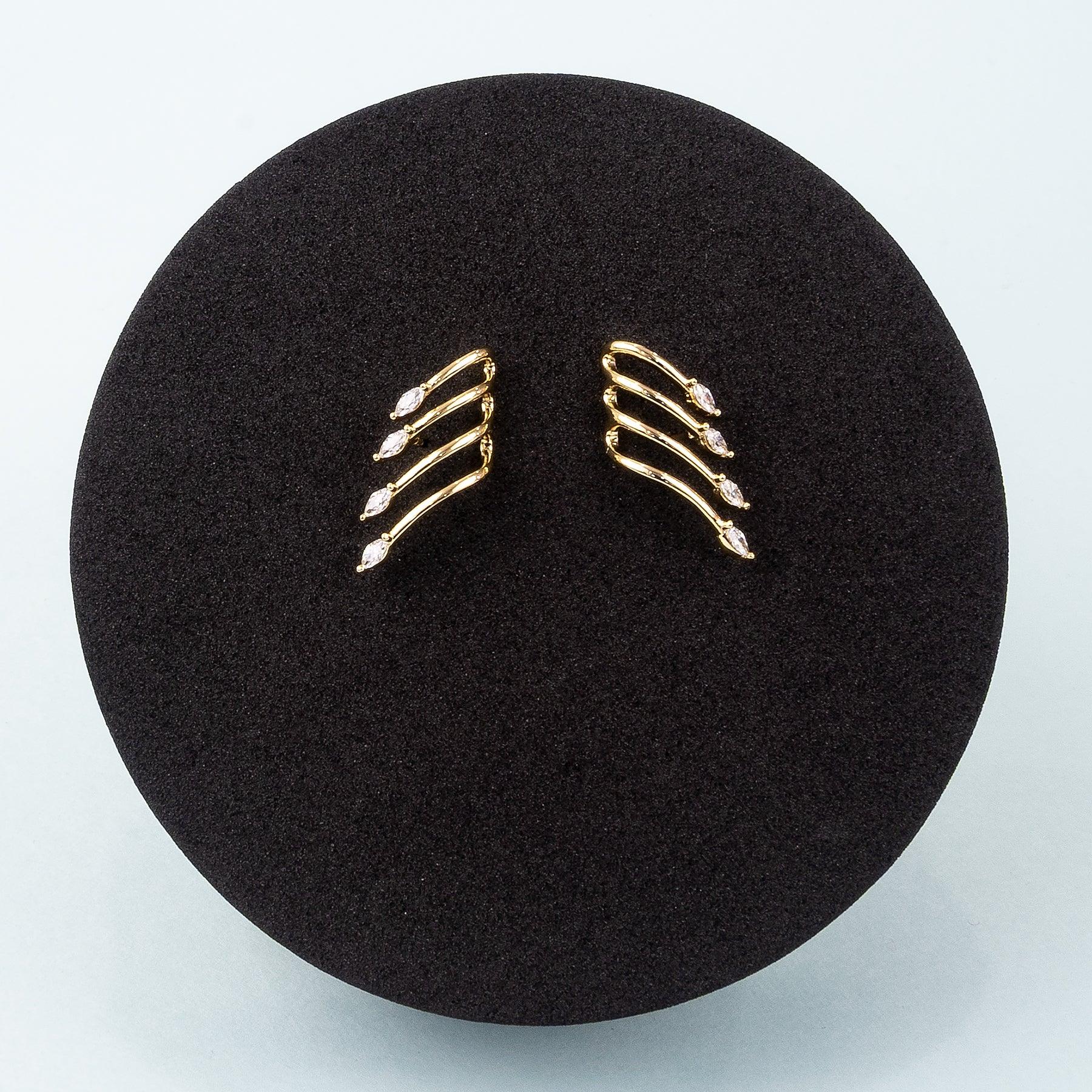 Gold earrings on a black round cushion with a light gray background