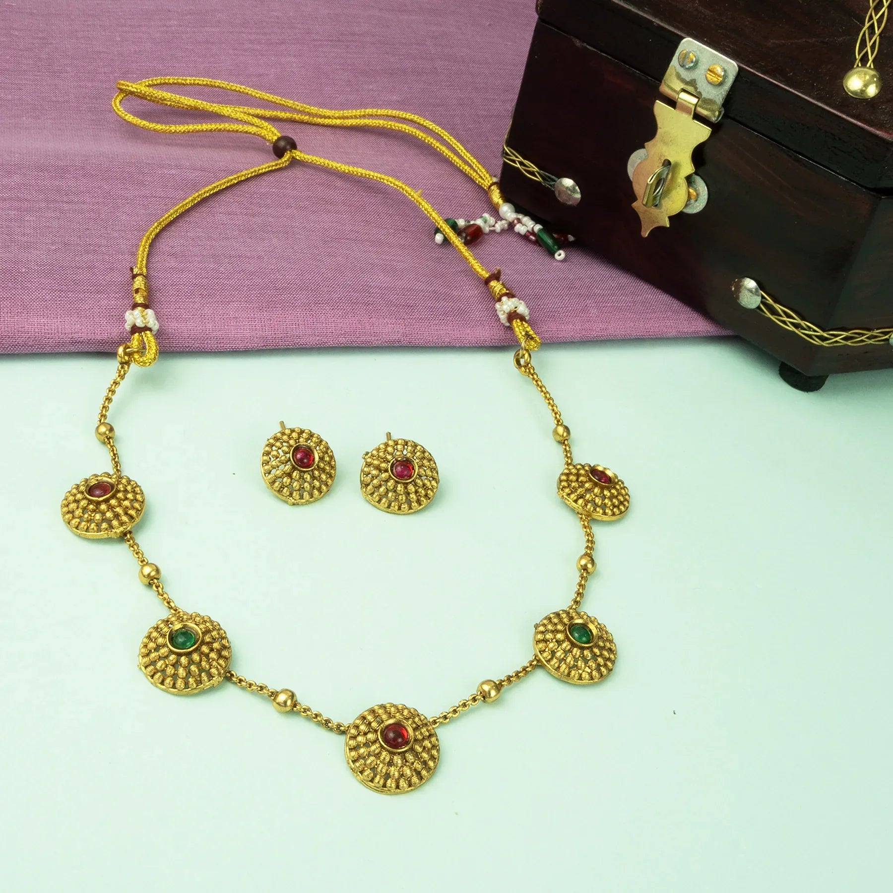 Gold necklace and earrings set on a light green surface with a purple fabric background