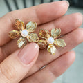 Gold flower-shaped earrings with a pearl center held between fingers.