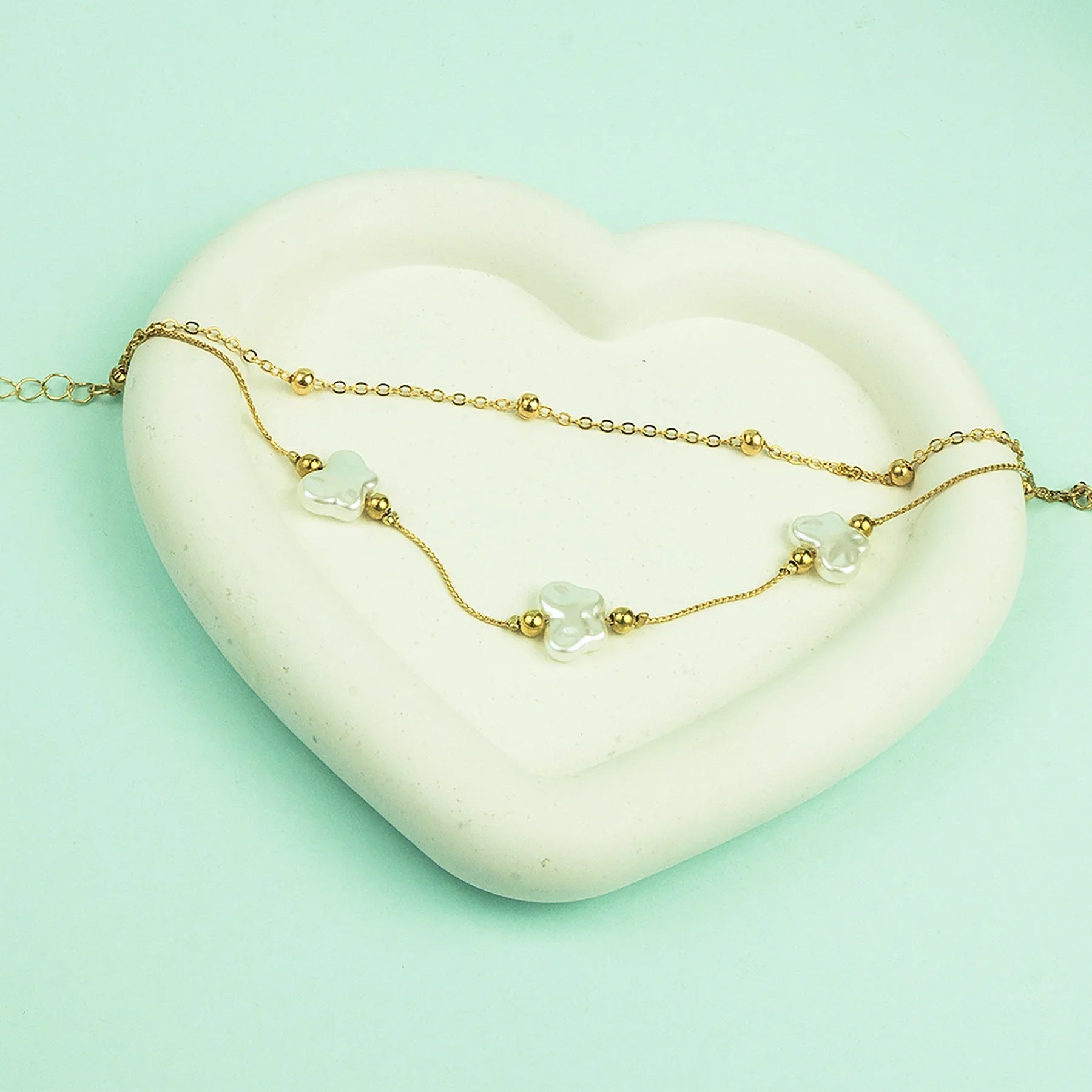 Gold bracelet with clear beads on a heart-shaped stone against a light green background