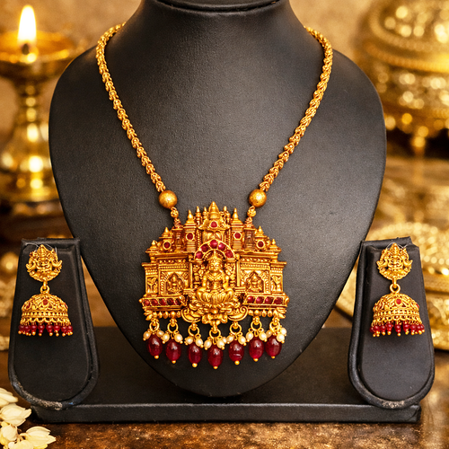 Gold necklace with temple design and red stones on a black stand, surrounded by similar jewelry.