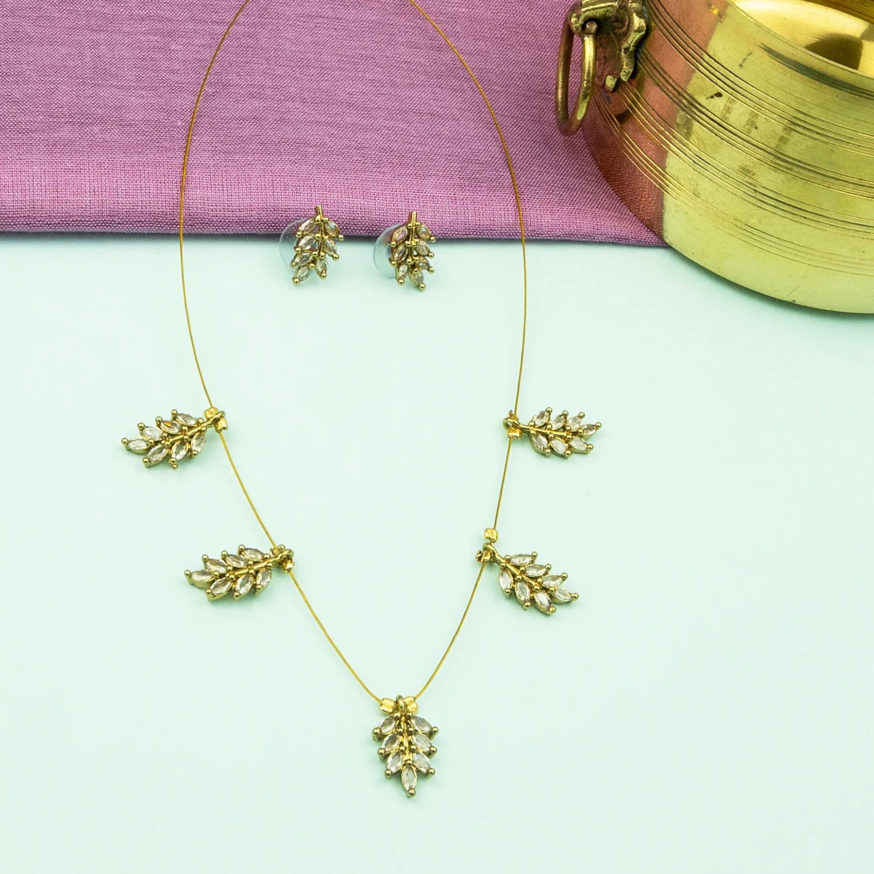 Gold necklace and earrings on a light green surface with a pink fabric background