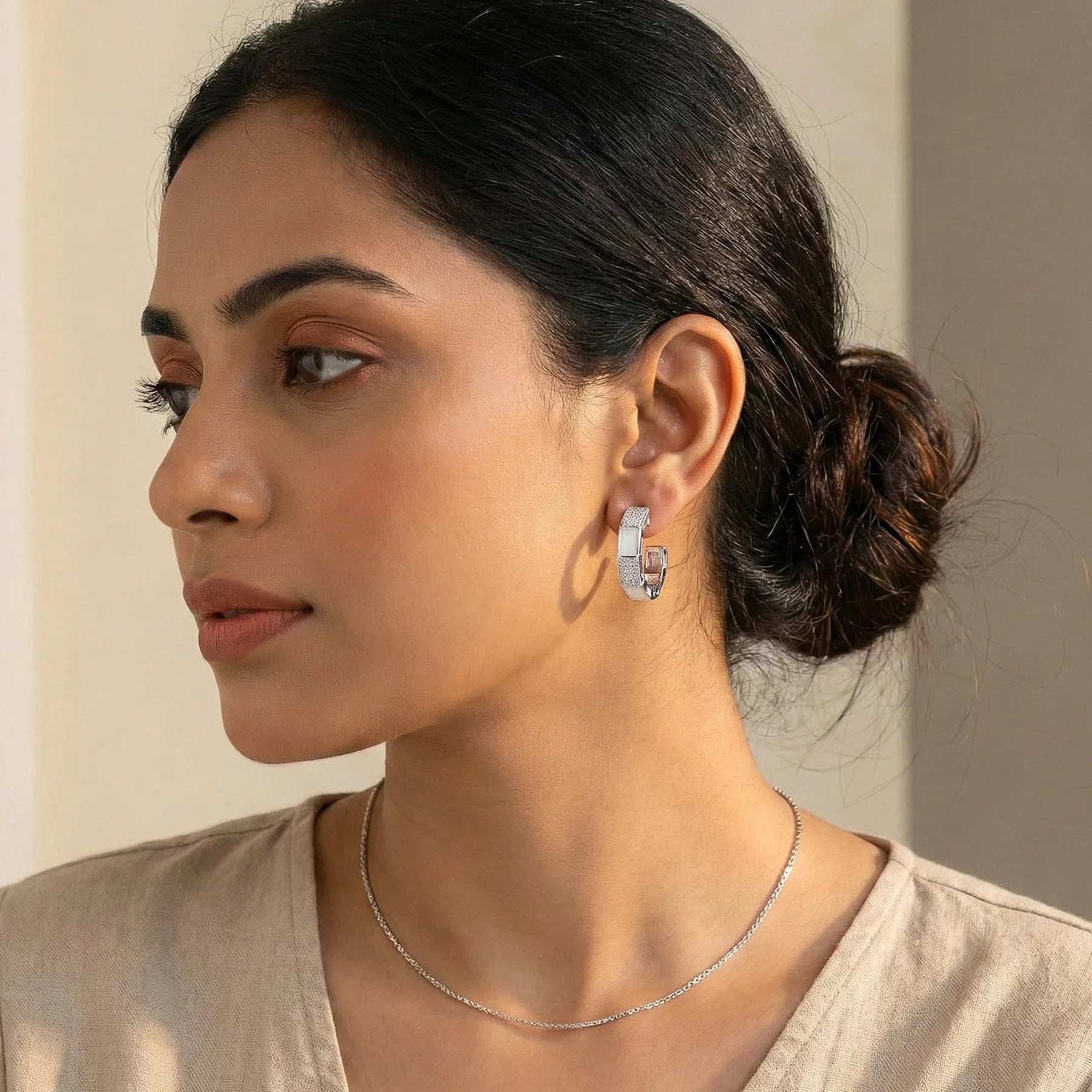 Woman wearing silver hoop earrings and a necklace against a neutral background