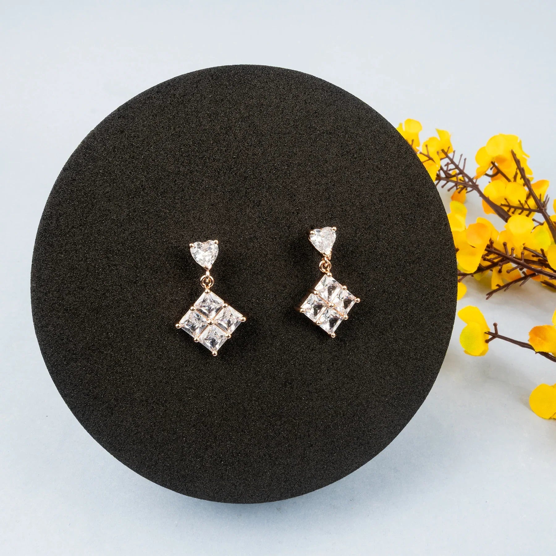 Pair of diamond earrings on a black round stand with yellow flowers in the background