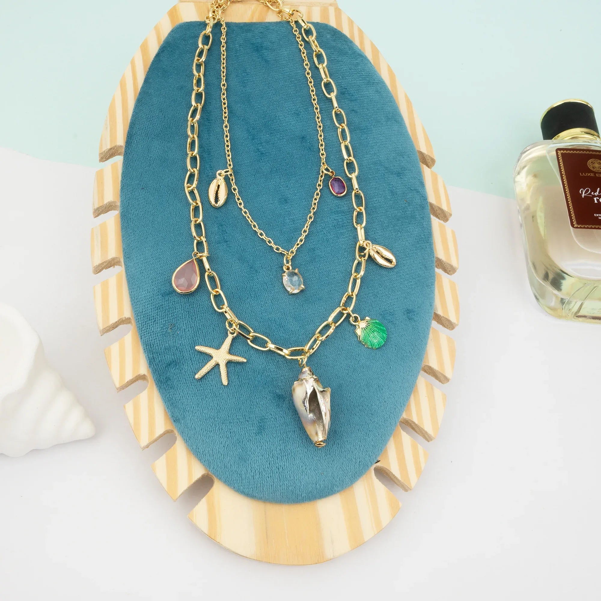 Gold necklace with charms on a blue and gold jewelry stand with a bottle of perfume in the background.