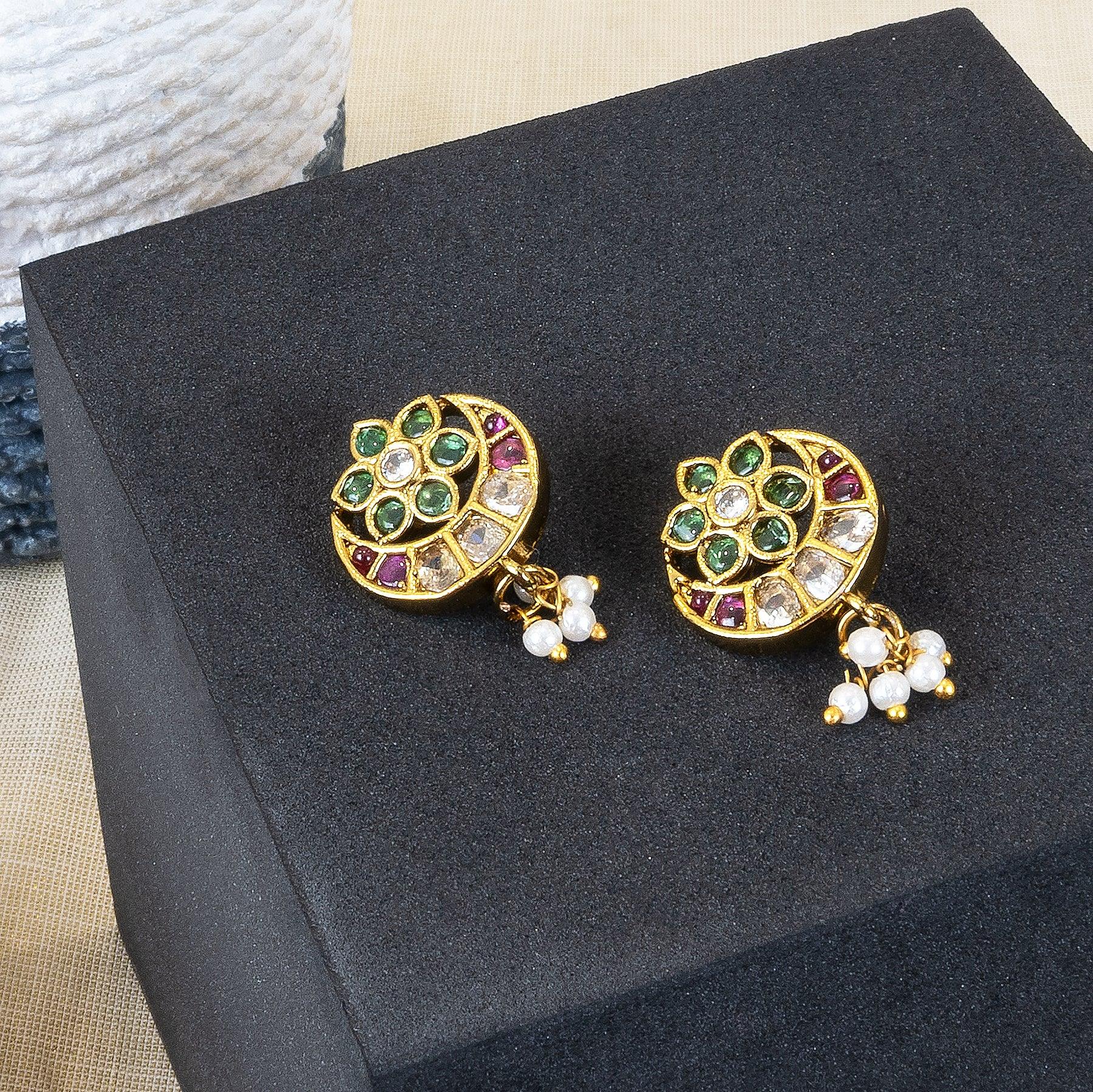 Pair of gold earrings with gemstones and pearls on a black stand.