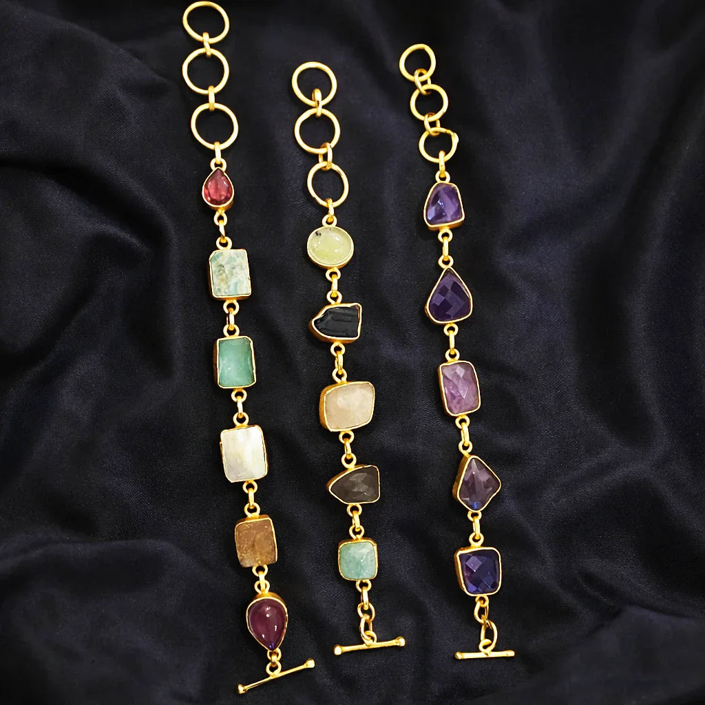 Gold necklaces with colorful gemstones on a dark fabric background