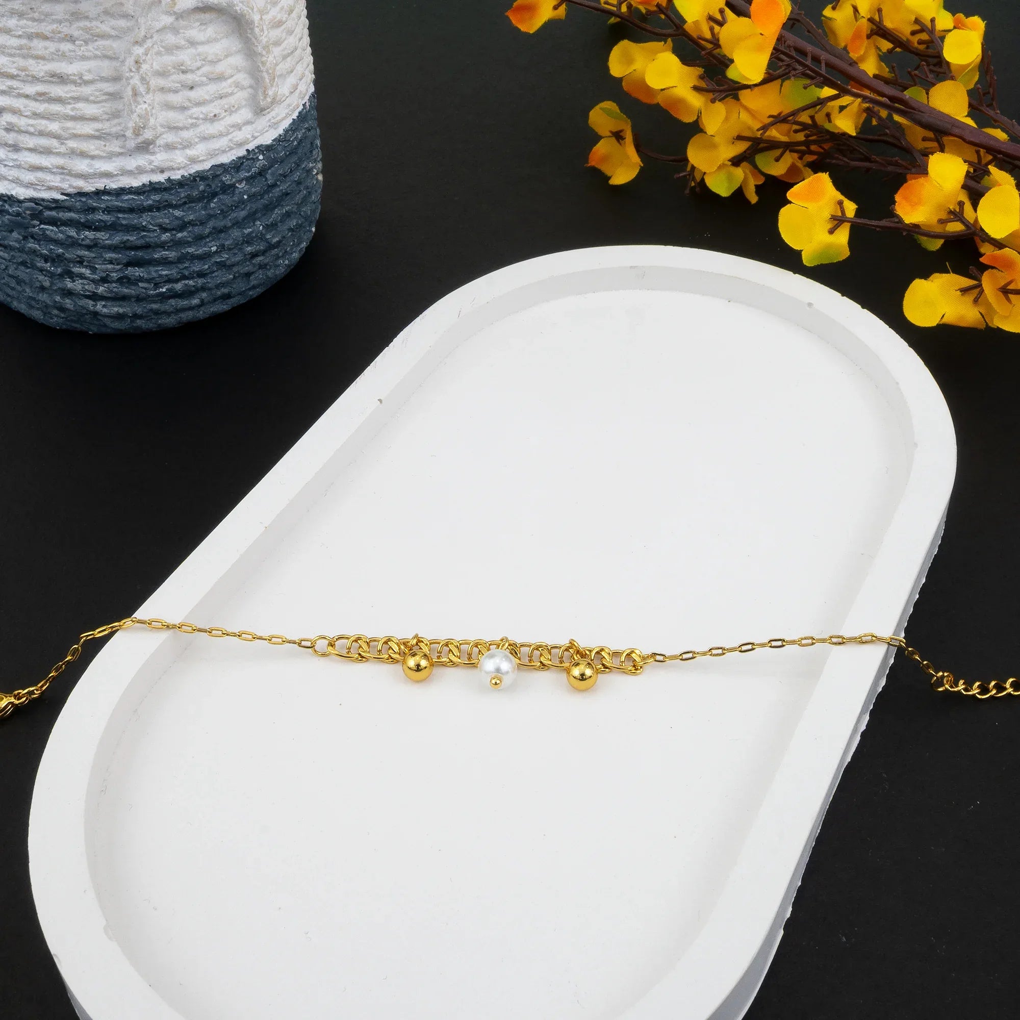 Gold bracelet with a pearl on a white dish with yellow flowers in the background