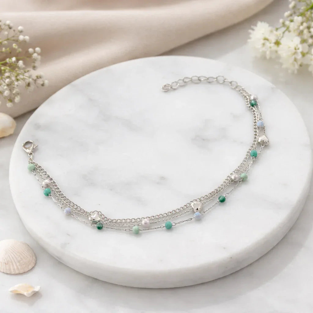 Silver necklace with green beads on a marble surface with flowers and shells.