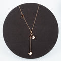 Rose gold necklace with heart and butterfly pendants on a black stand.