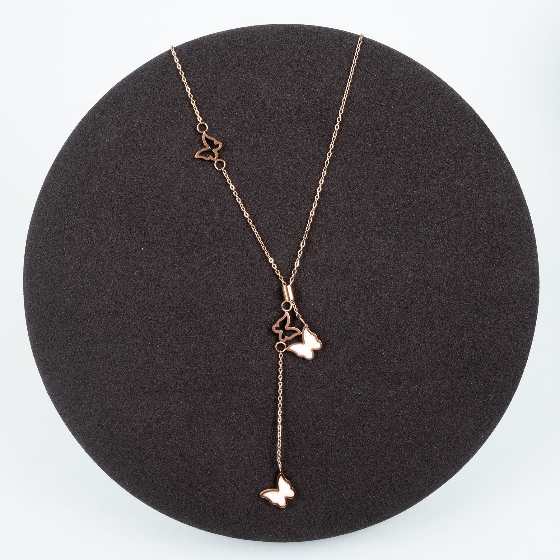 Rose gold necklace with heart and butterfly pendants on a black stand.