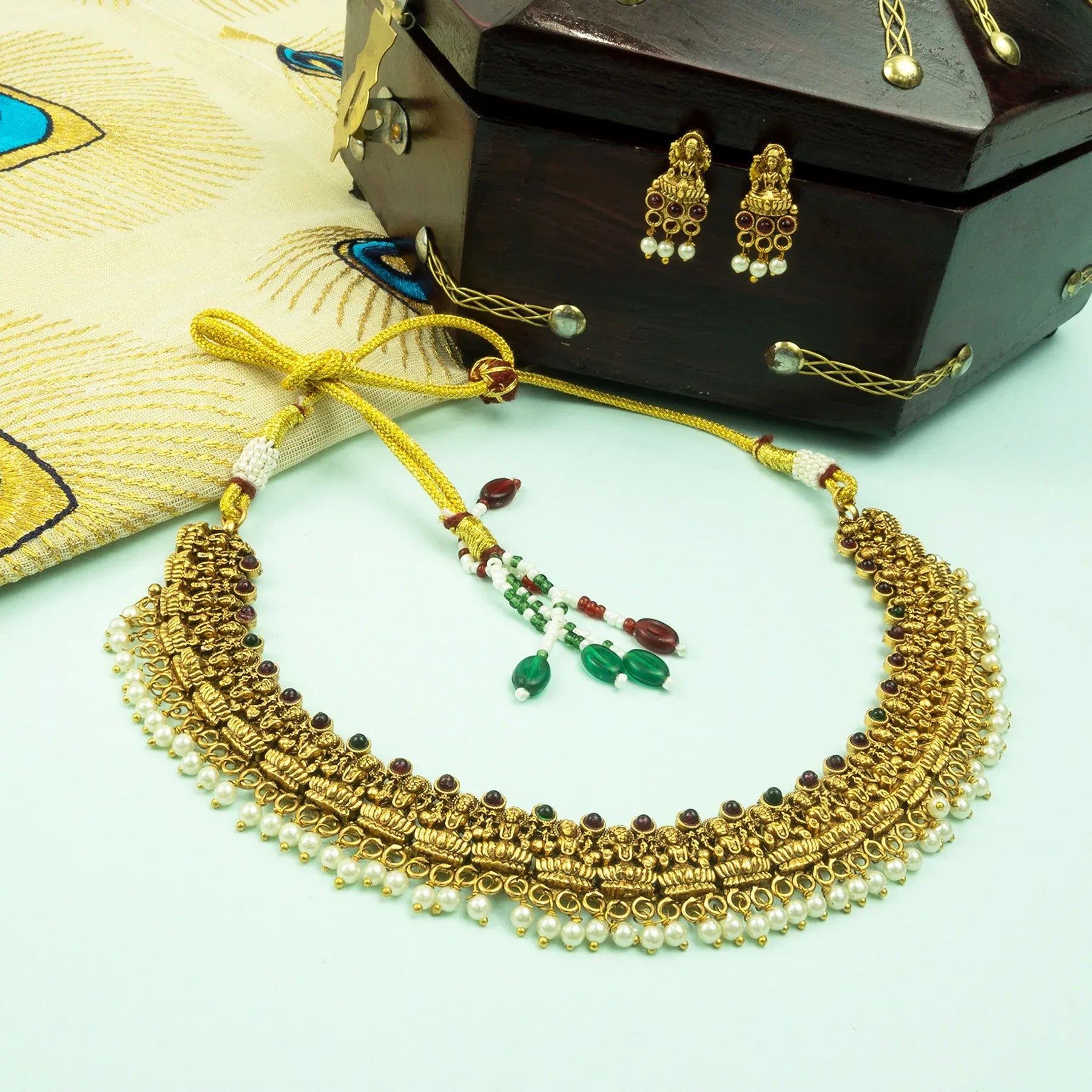 Gold necklace with pearls and green stones on a light blue background