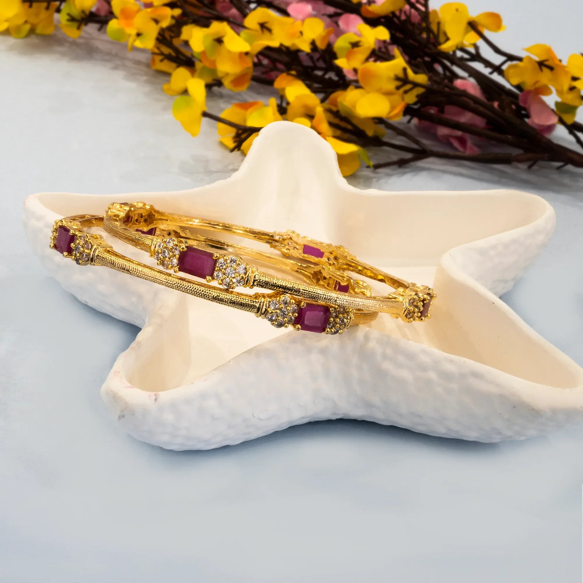 Gold bracelets with purple stones on a starfish with yellow flowers in the background