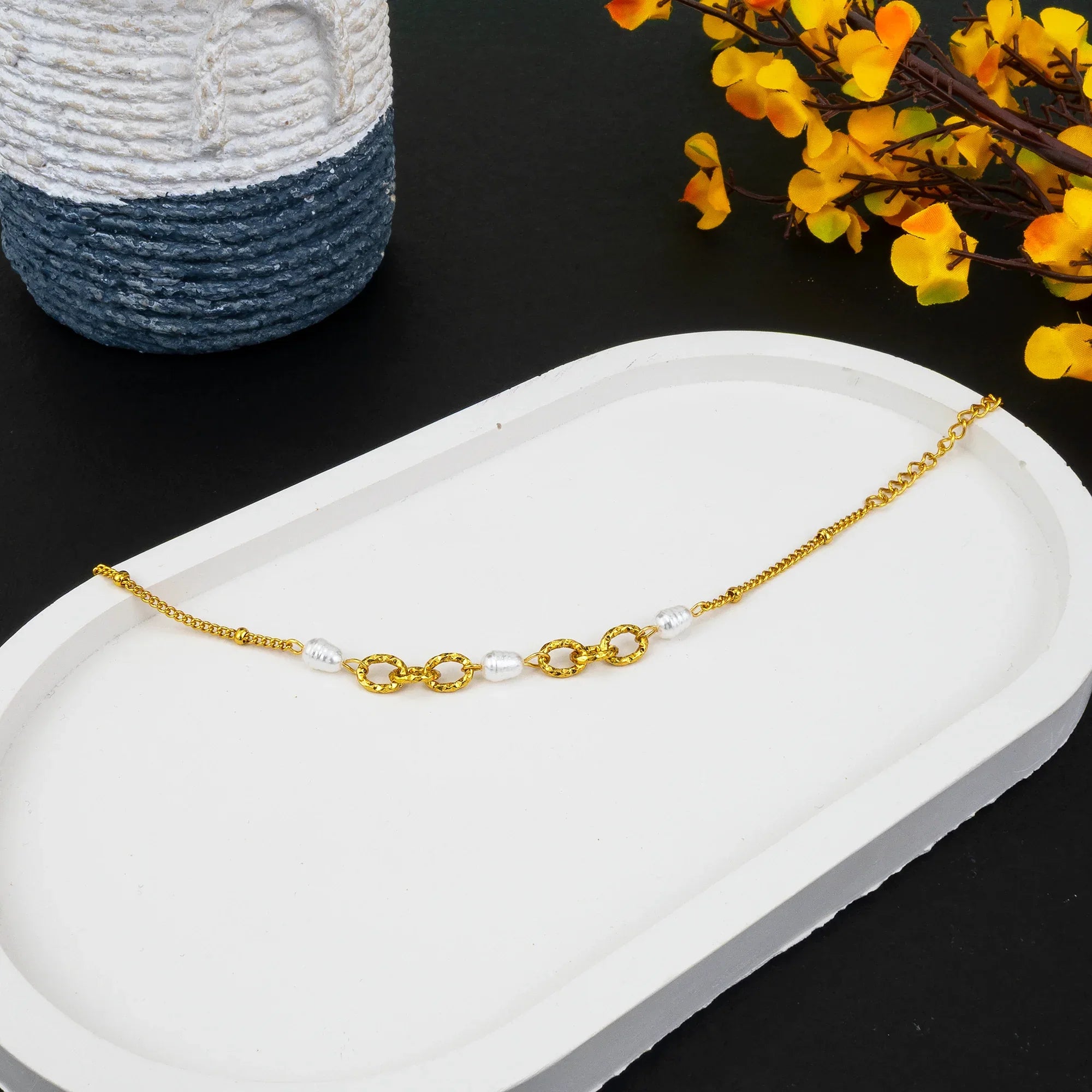 Gold bracelet with pearls on a white tray with a black background and yellow flowers.