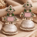 Ornate silver earrings with green gemstones and pink stones on a beige fabric background