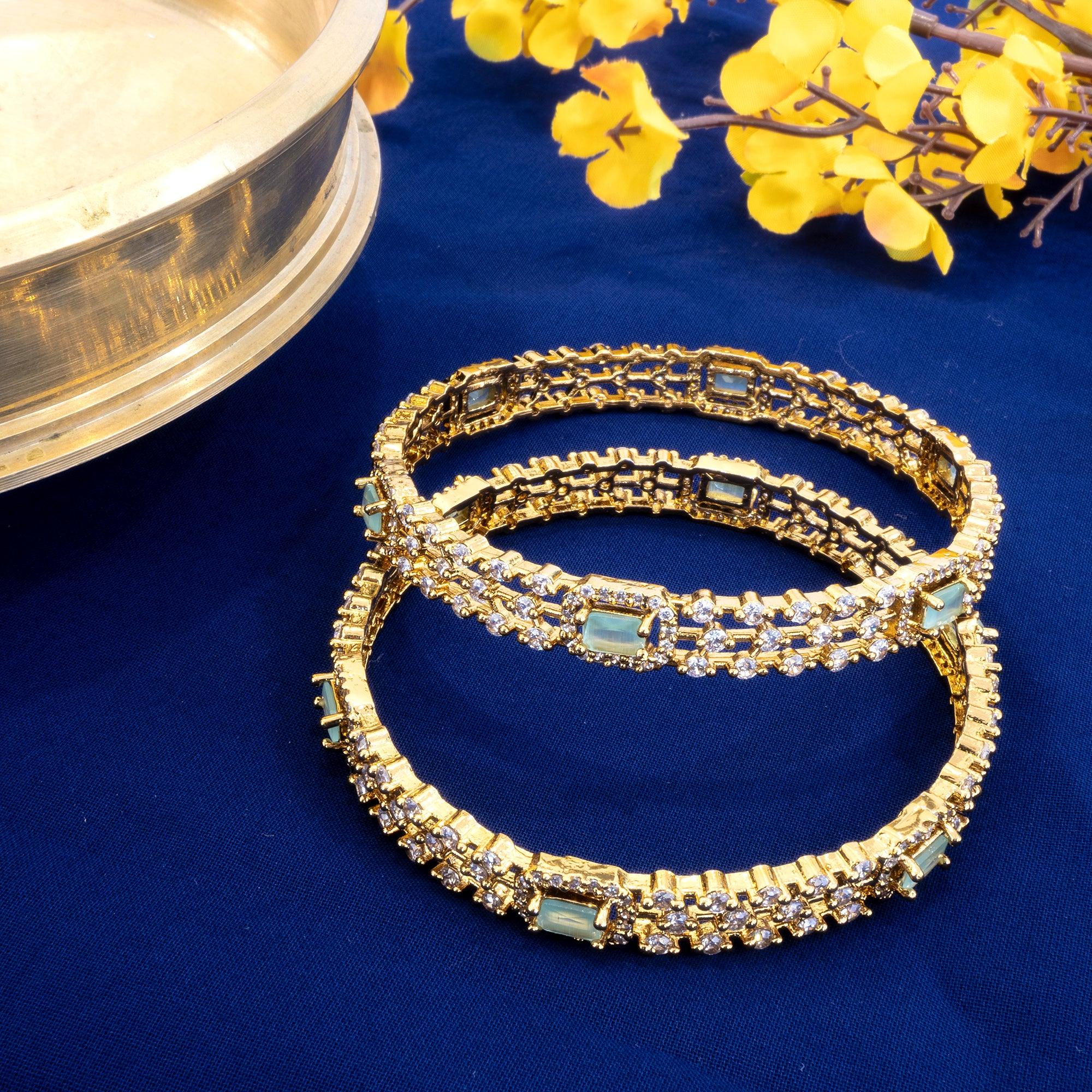 Gold bracelets with gemstones on a blue surface with yellow flowers.