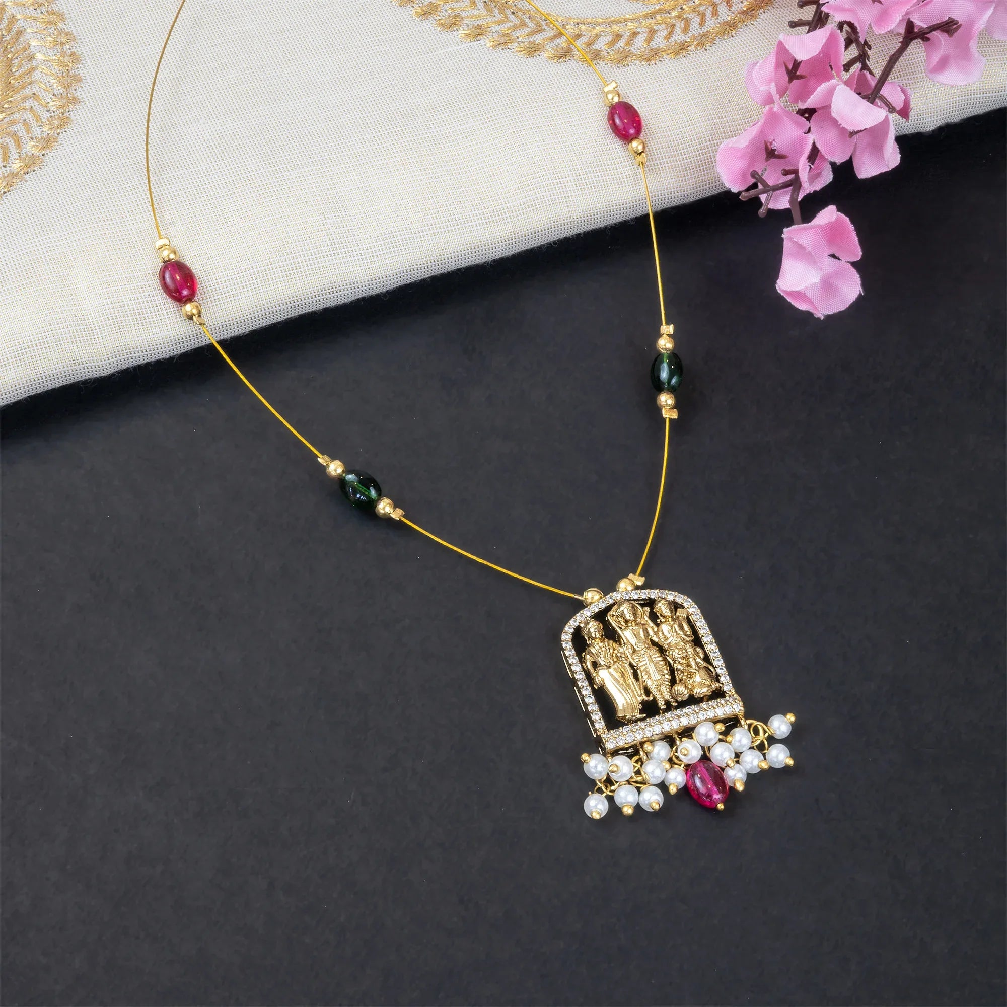 Decorative necklace with a pendant on a dark surface with pink flowers.