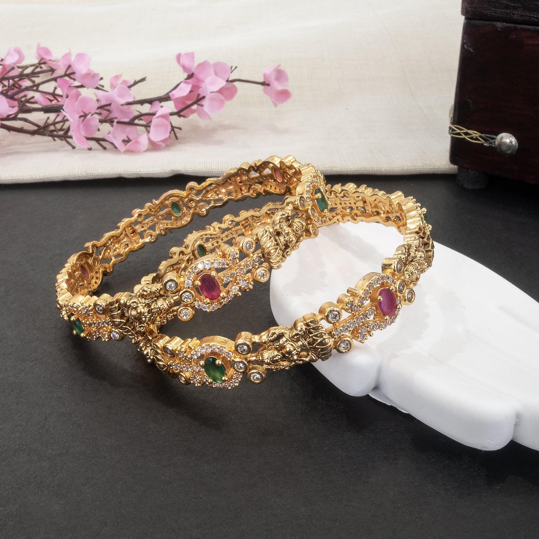 Gold bracelet with gemstones on a white hand model, with pink flowers in the background.