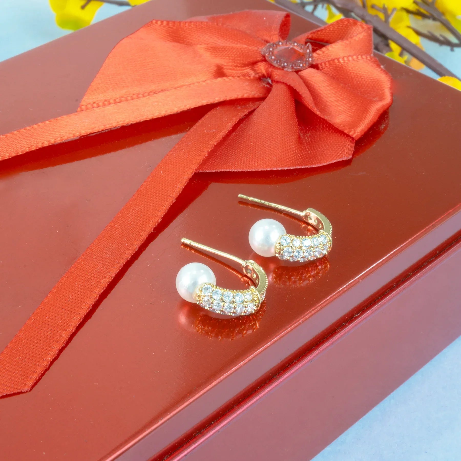 Gold and pearl earrings on a red box with an orange ribbon