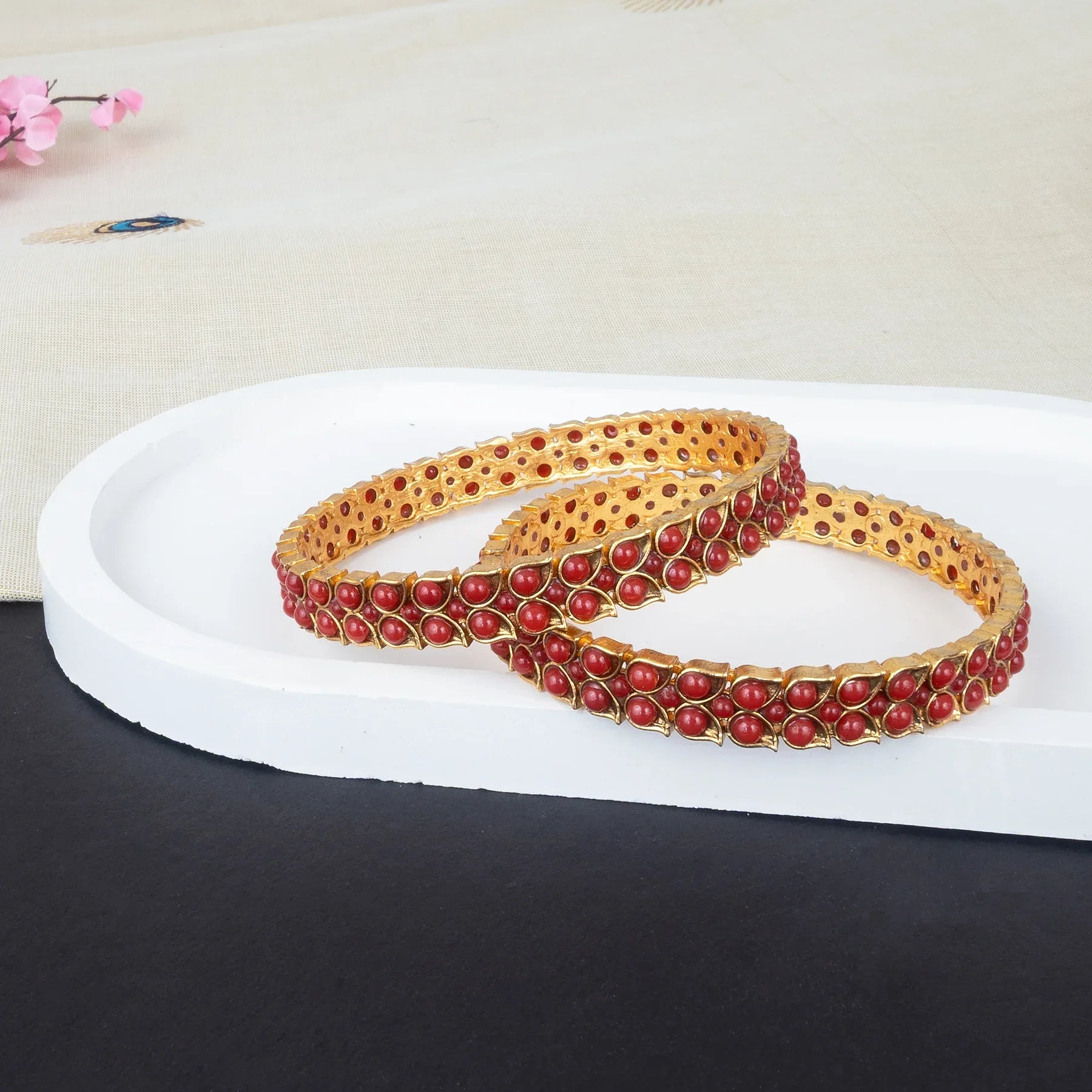 Pair of gold and red beaded bracelets on a white platform with a light background