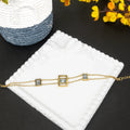 Gold bracelet with square stones on a white jewelry box with yellow flowers in the background