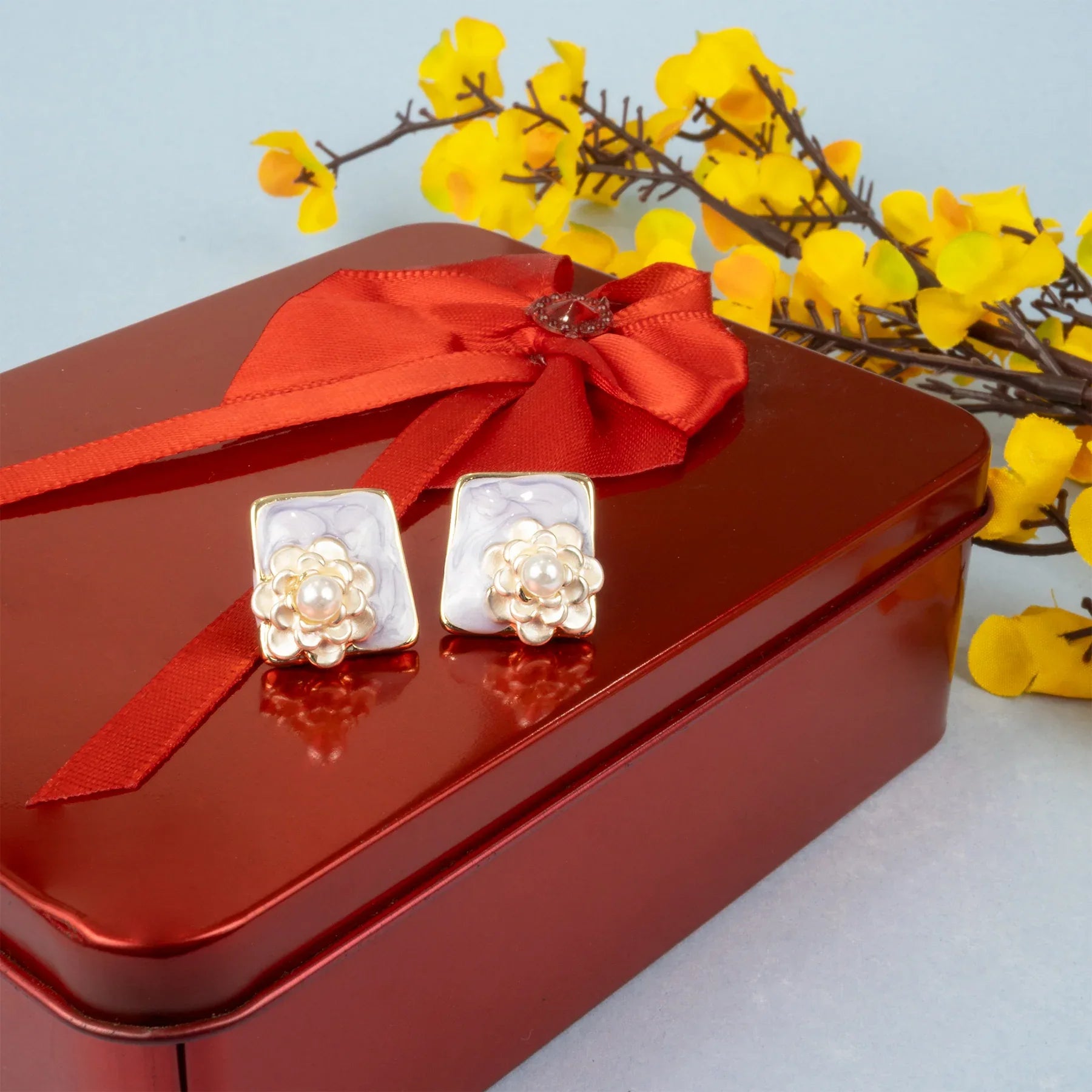 Pair of earrings on a red box with a red ribbon and yellow flowers in the background