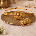Gold necklace and earrings set on a decorative plate with a soft background