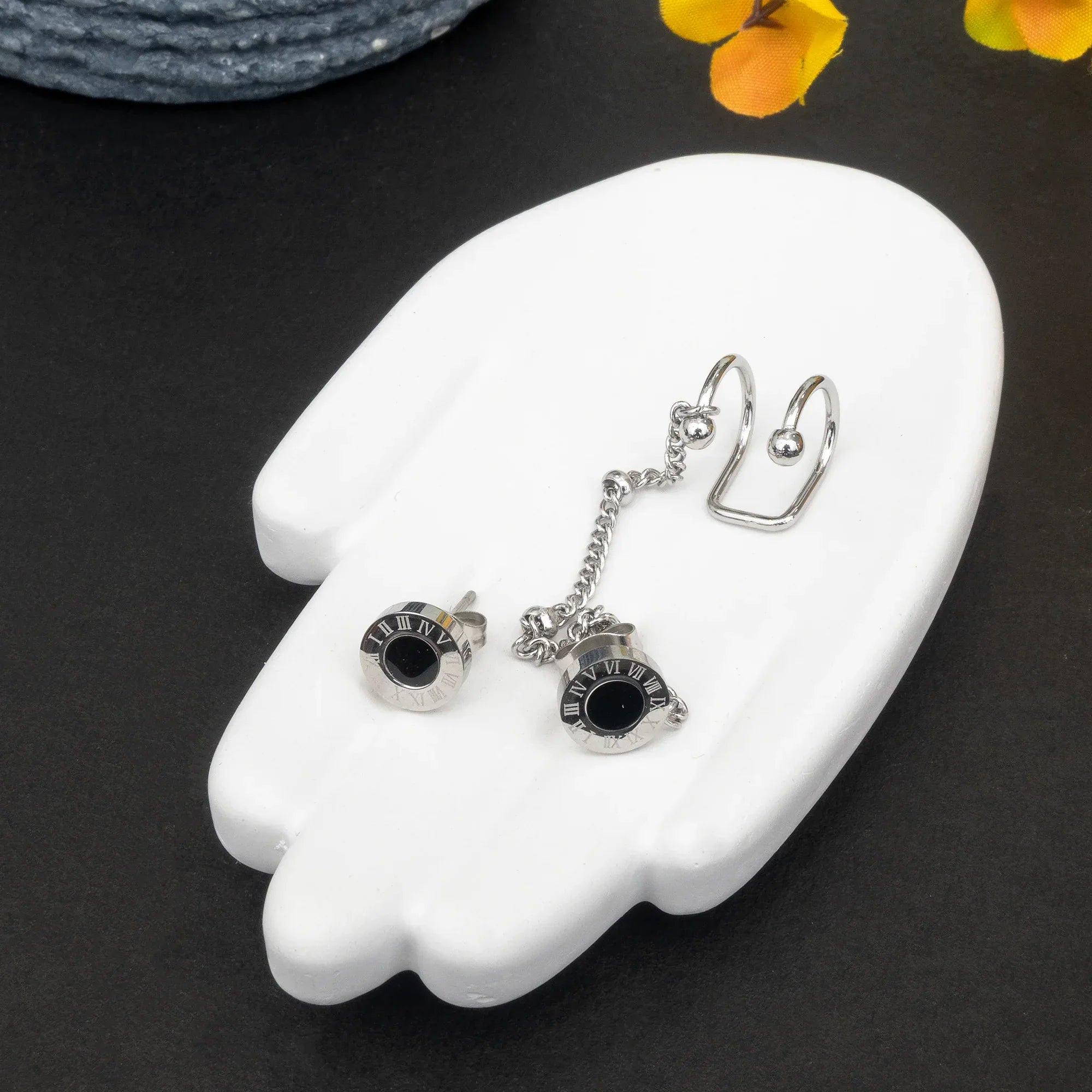 Pair of silver earrings with black stones on a white hand-shaped stand against a dark background.
