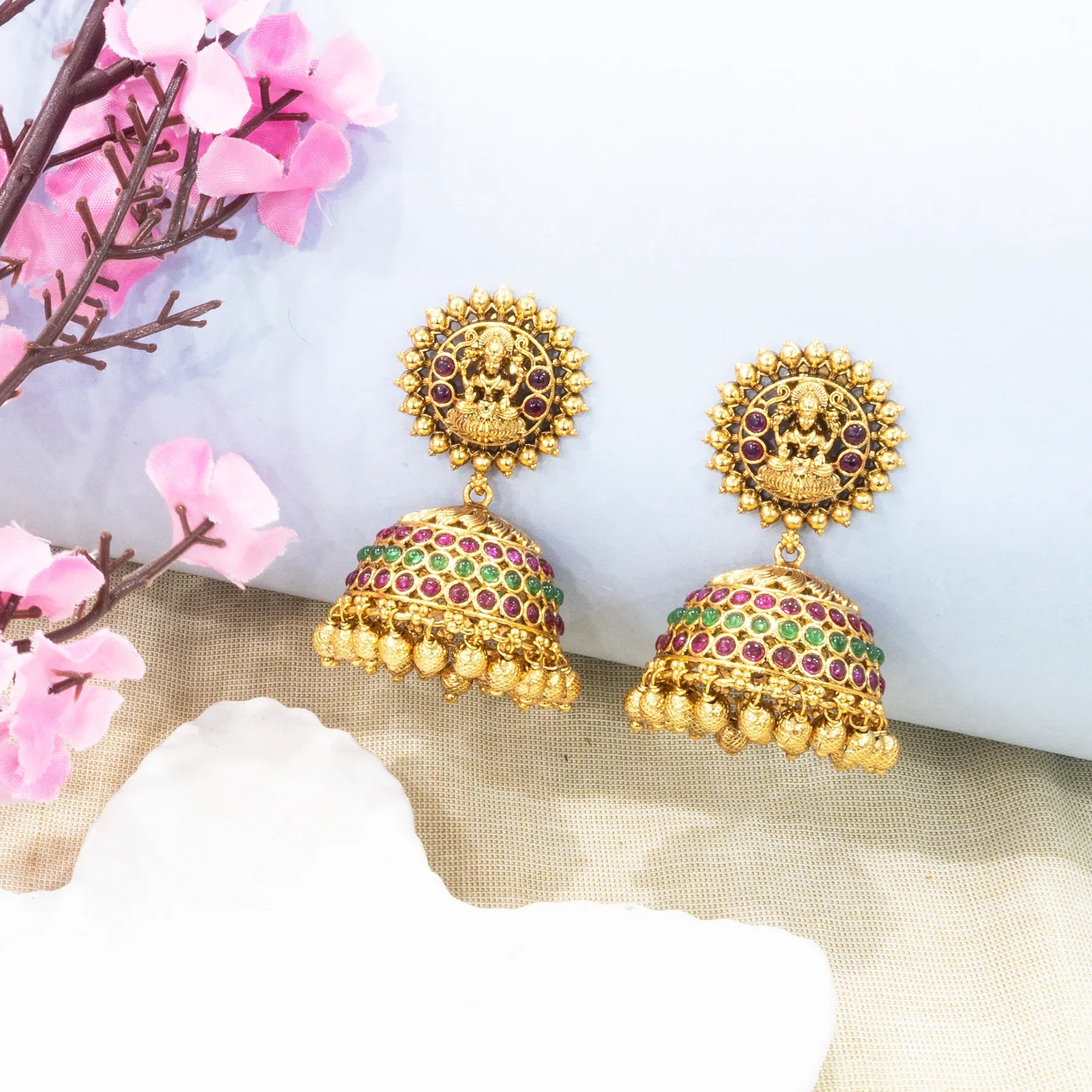 Gold earrings with gemstones on a decorative background with pink flowers