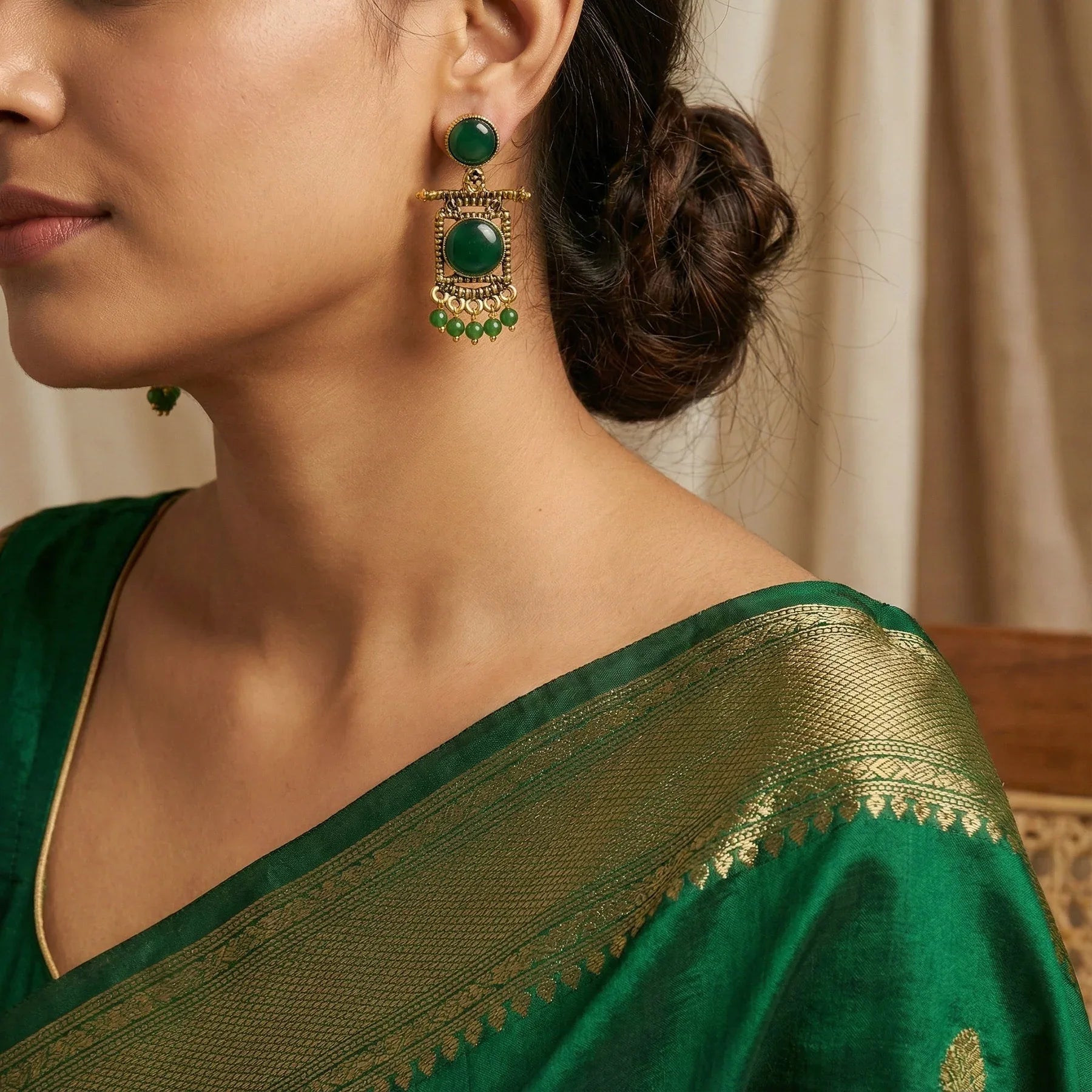 Woman wearing a green saree with gold border and green earrings.