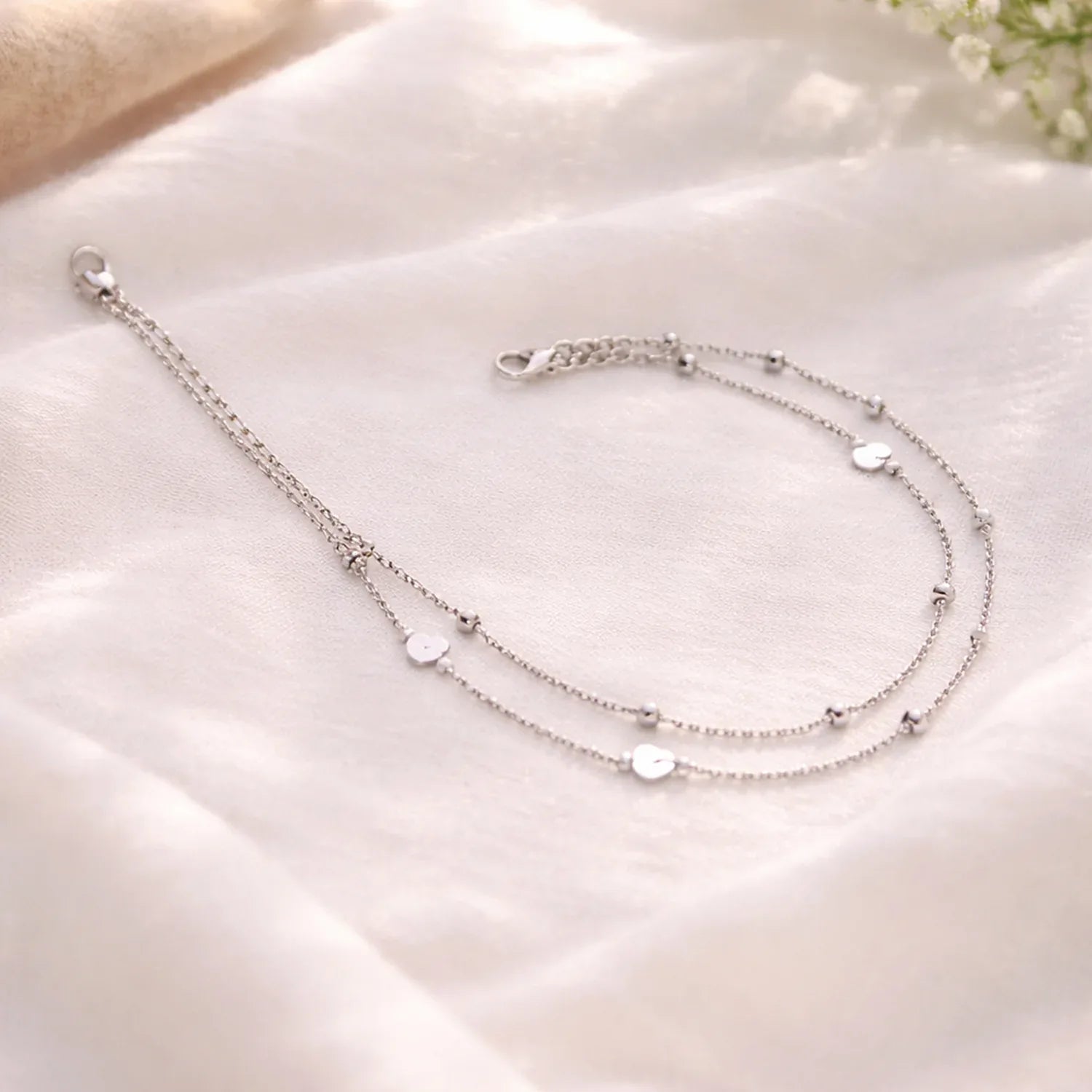 Silver anklets on a soft white fabric background