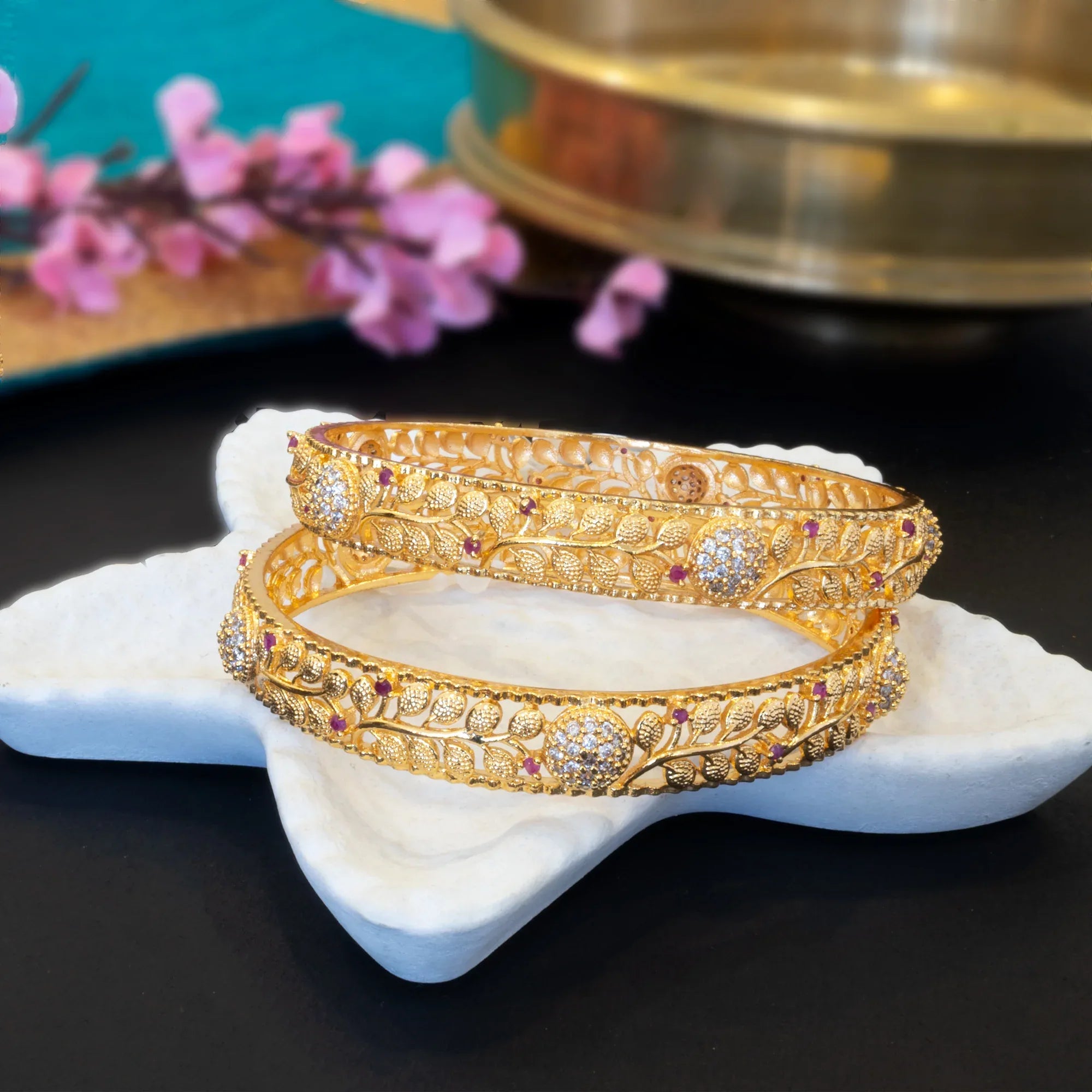 Gold bangles with gemstones on a white stone surface with a blurred background