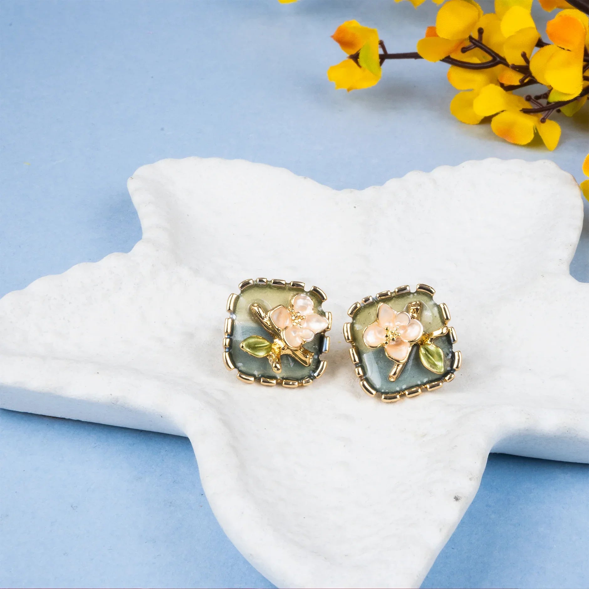 Pair of floral earrings on a starfish with yellow flowers in the background
