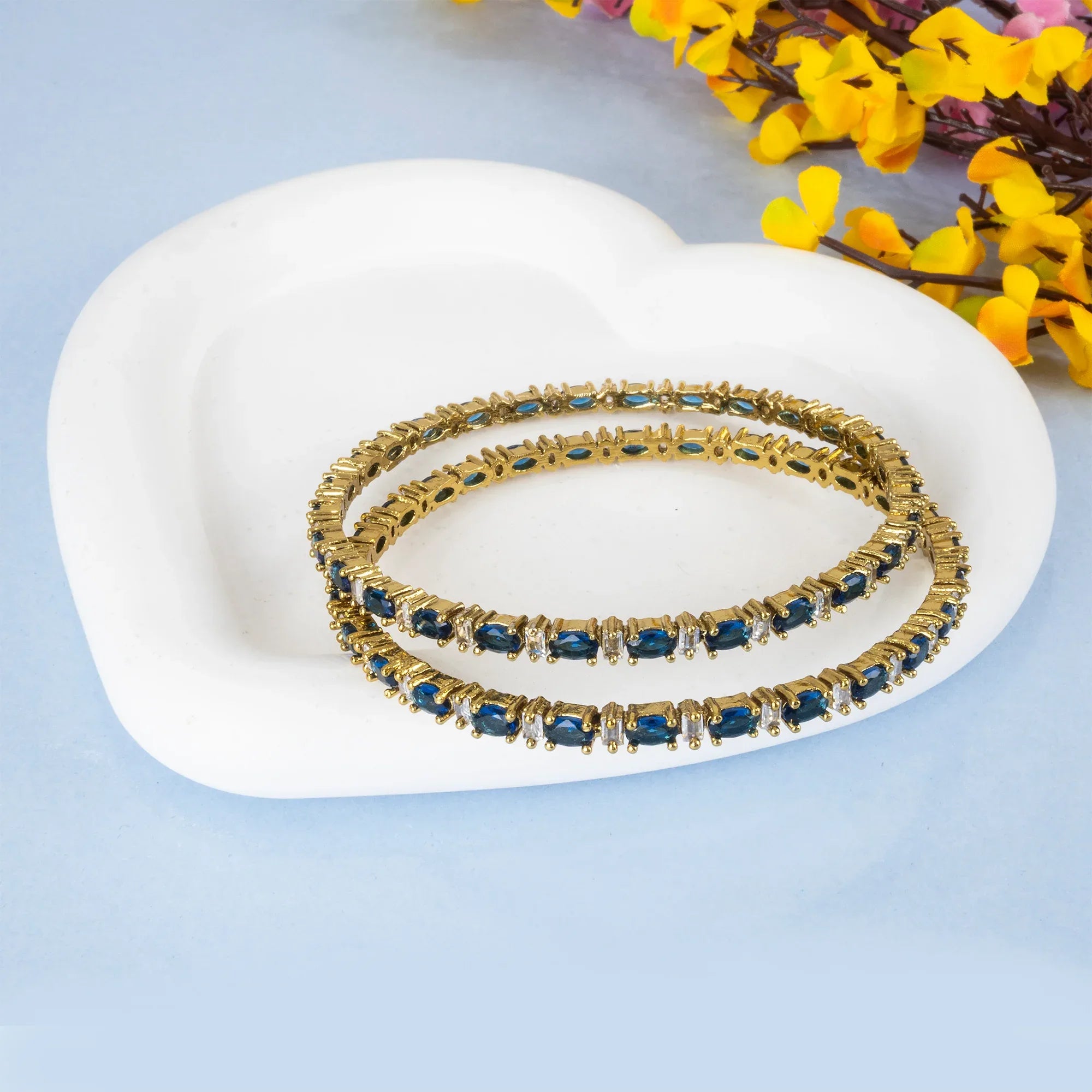 Gold and blue bracelet on a white dish with flowers in the background