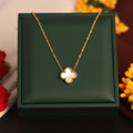 Gold necklace with a clover-shaped pendant on a green box with flowers in the background