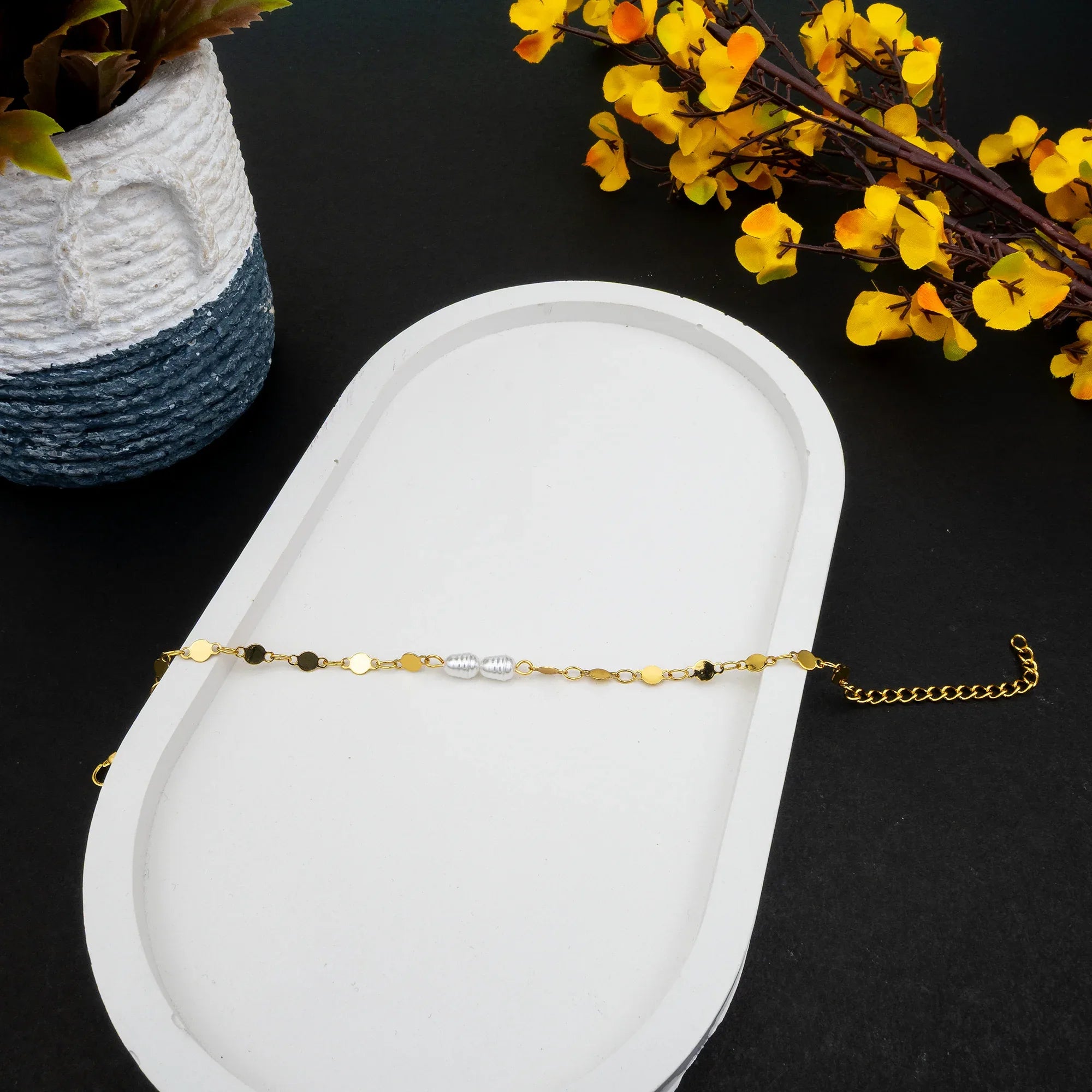 Gold bracelet on a white dish with yellow flowers and a woven basket in the background