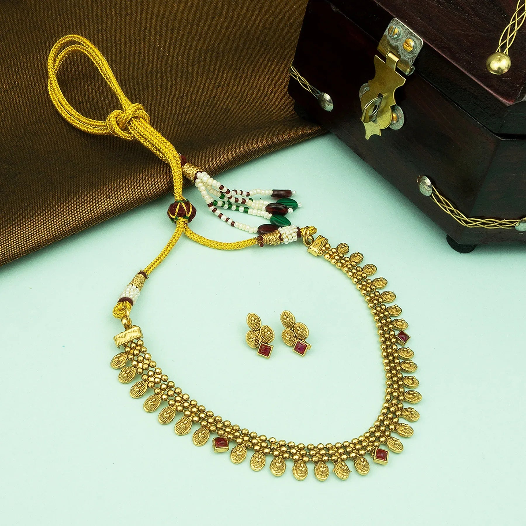 Gold necklace with red stones and matching earrings on a light green surface.