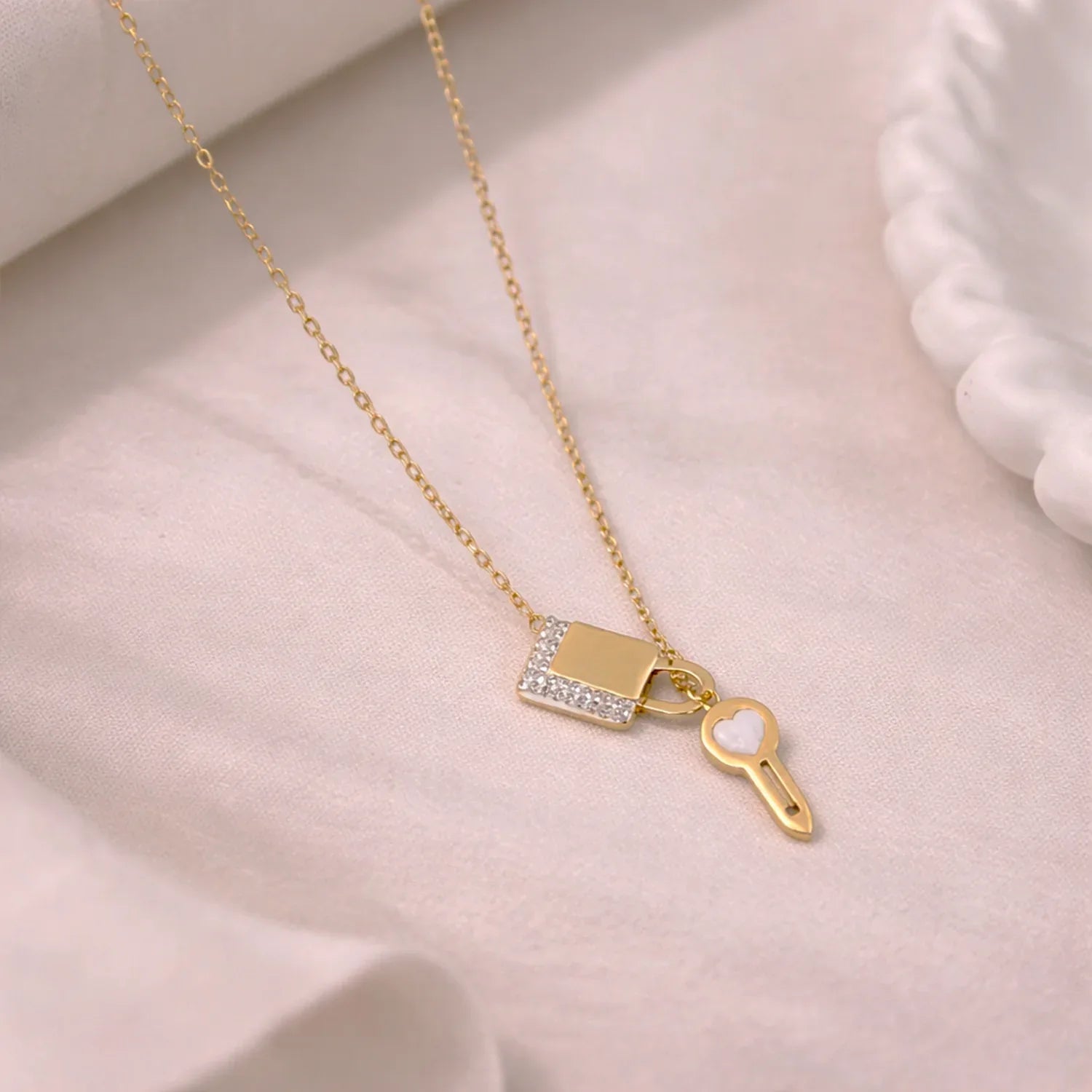 Gold necklace with lock and key pendant on a soft pink background