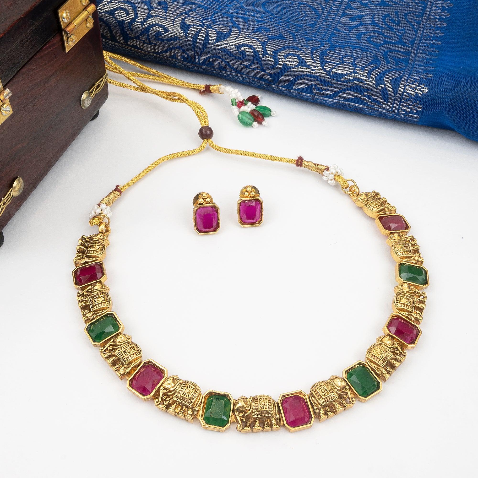 Gold necklace with colorful gemstones on a white surface with a blue fabric background