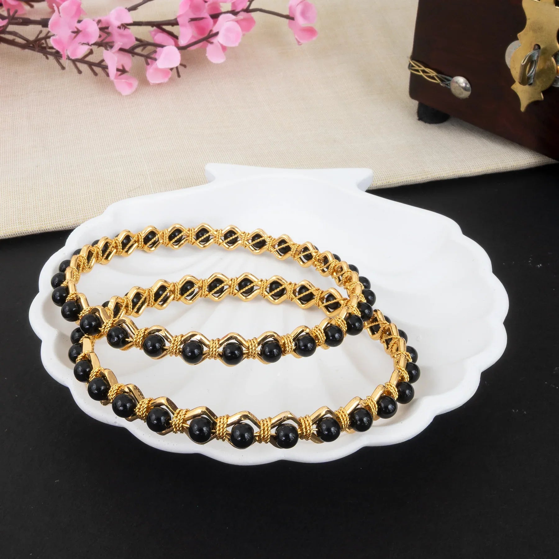 Gold and black beaded bracelets on a white dish with pink flowers in the background