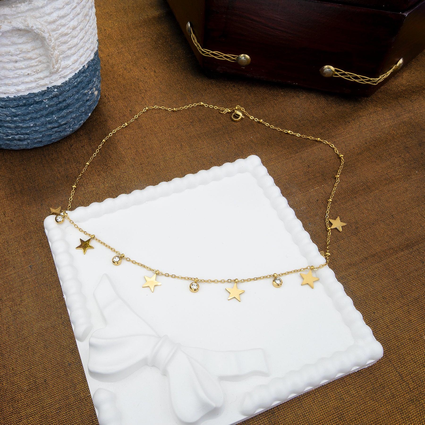 Gold necklace with star pendants on a white stand against a brown background