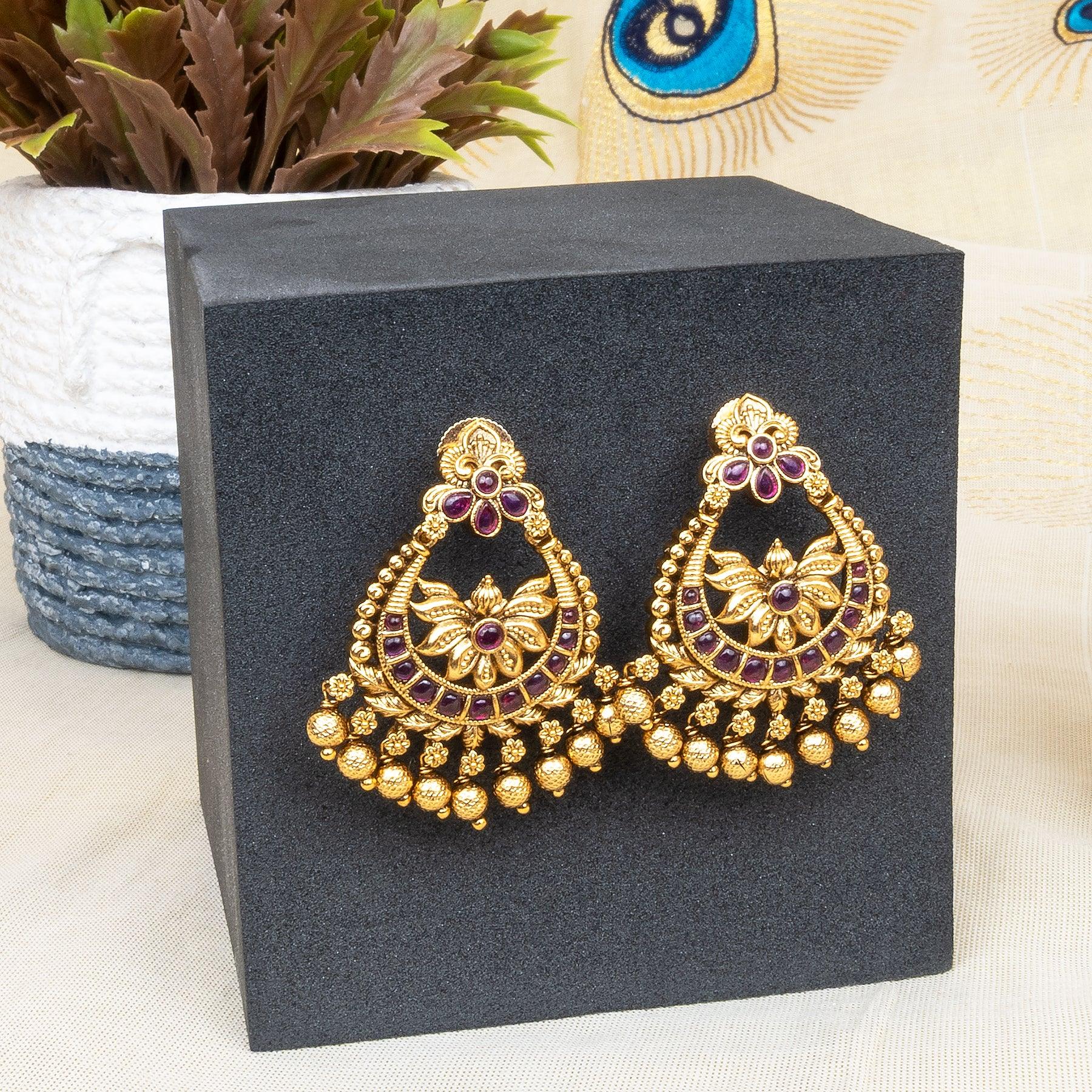 Gold earrings with purple stones on a black box with a decorative background