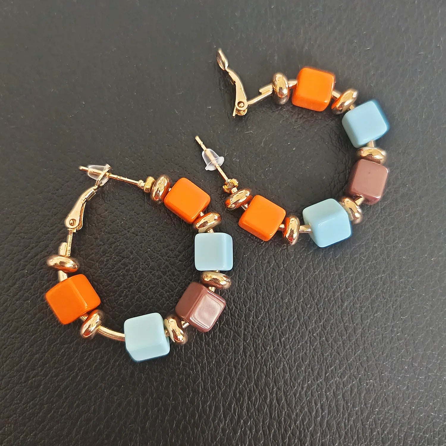 Colorful hoop earrings with square beads on a dark textured surface