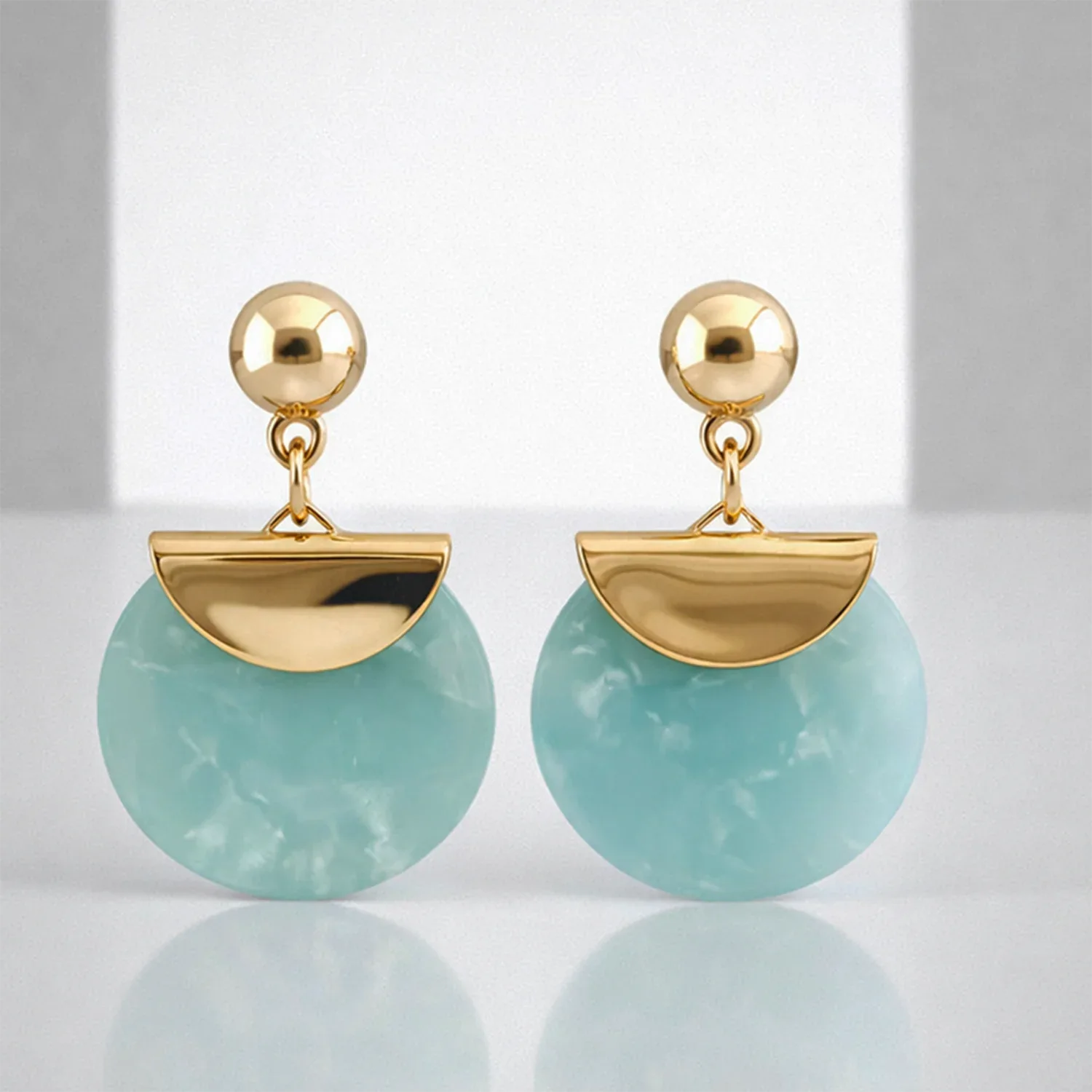Gold earrings with green circular stones on a reflective surface