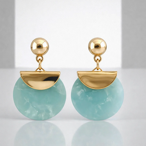 Gold earrings with green circular stones on a reflective surface