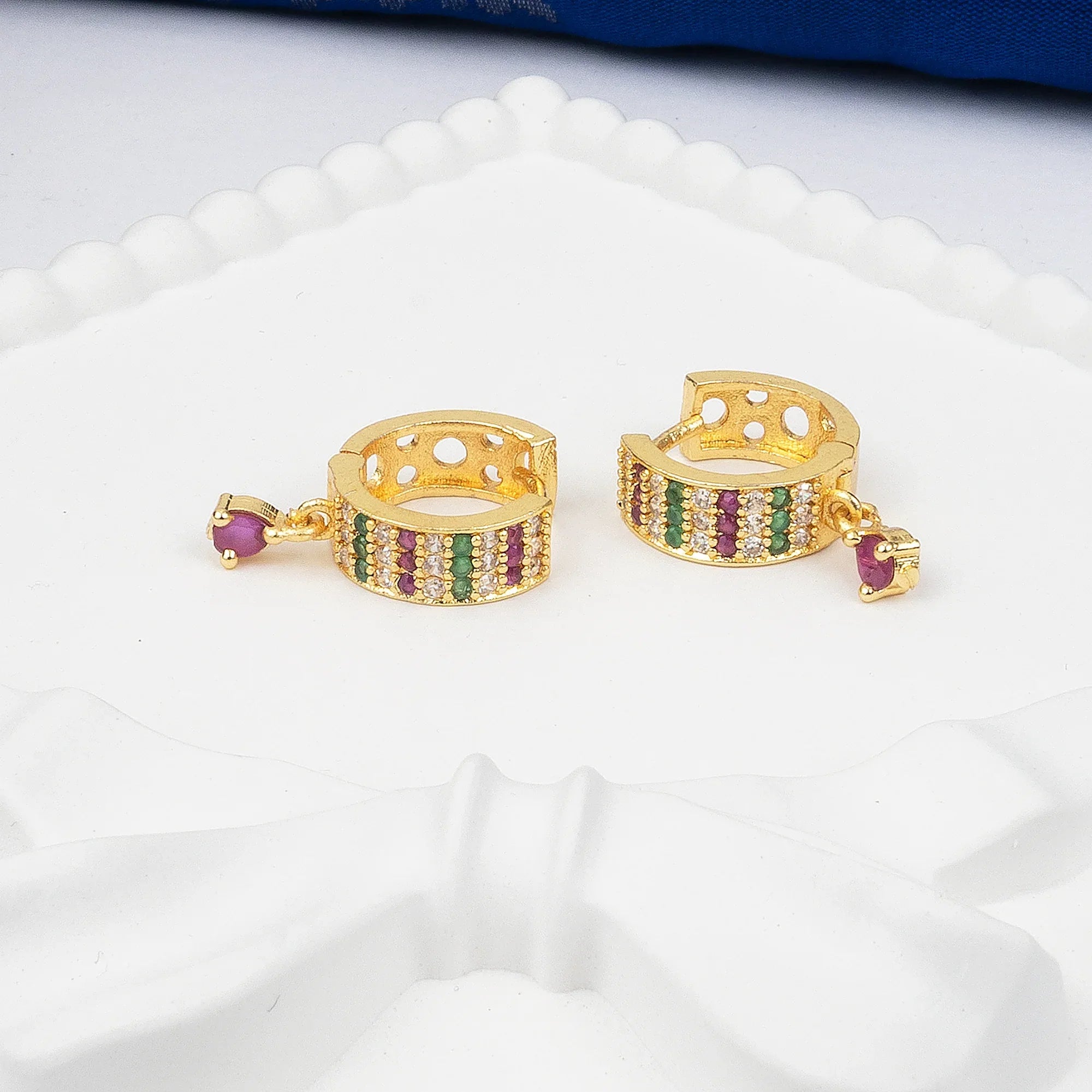 Gold hoop earrings with colorful gemstones on a white surface