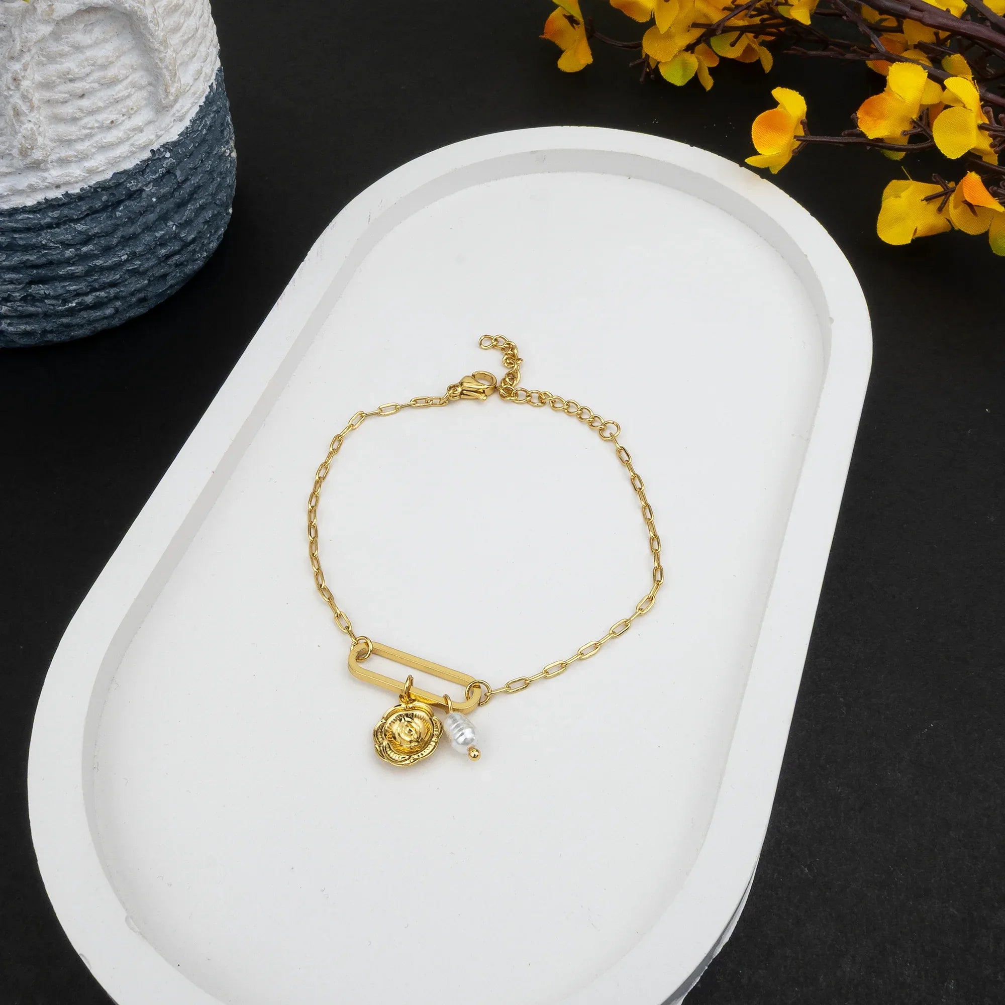 Gold bracelet with a pendant on a white tray with a black background