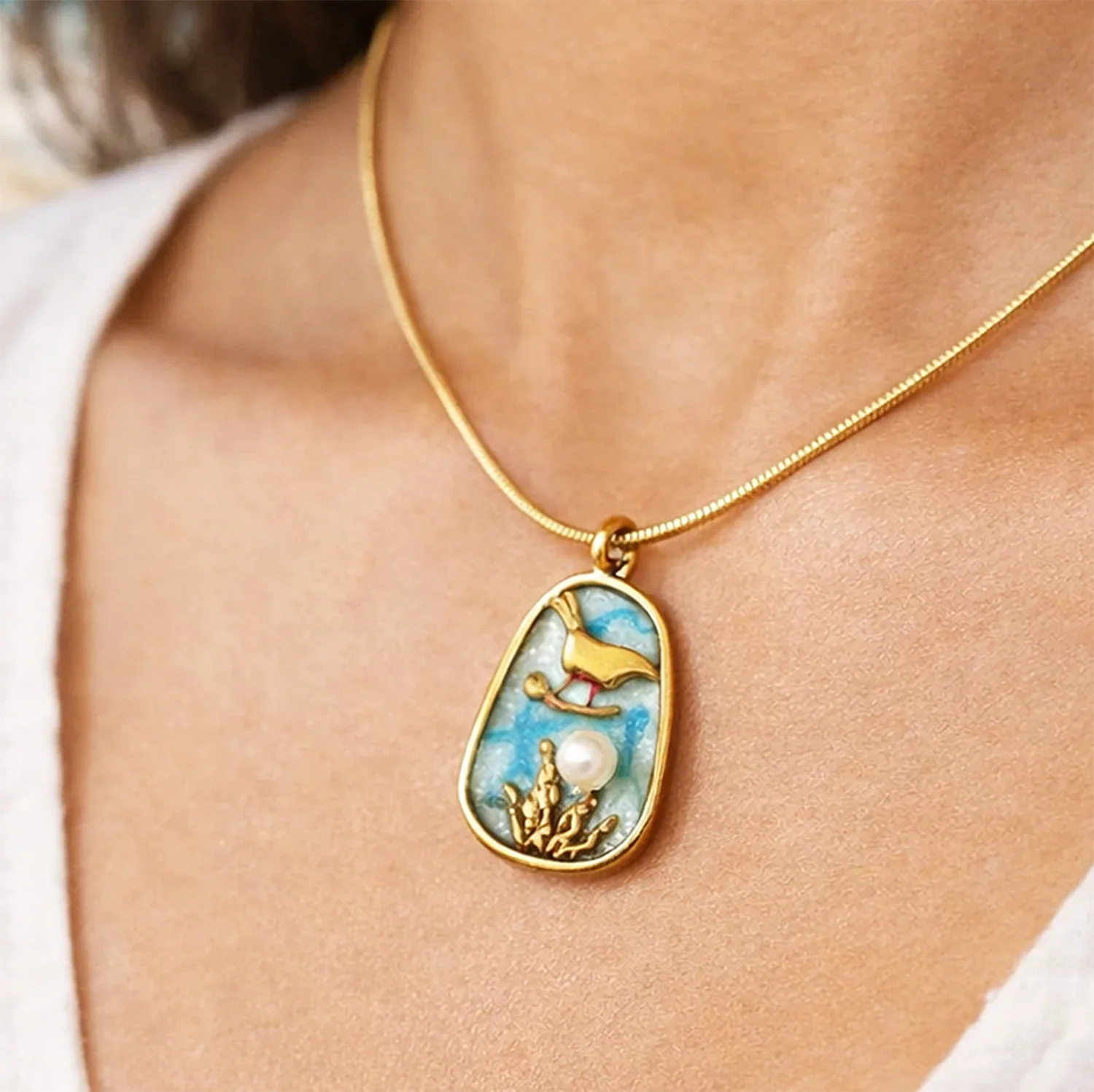 Necklace with a pendant featuring a design of a bird, pearl, and foliage on a person's neck.
