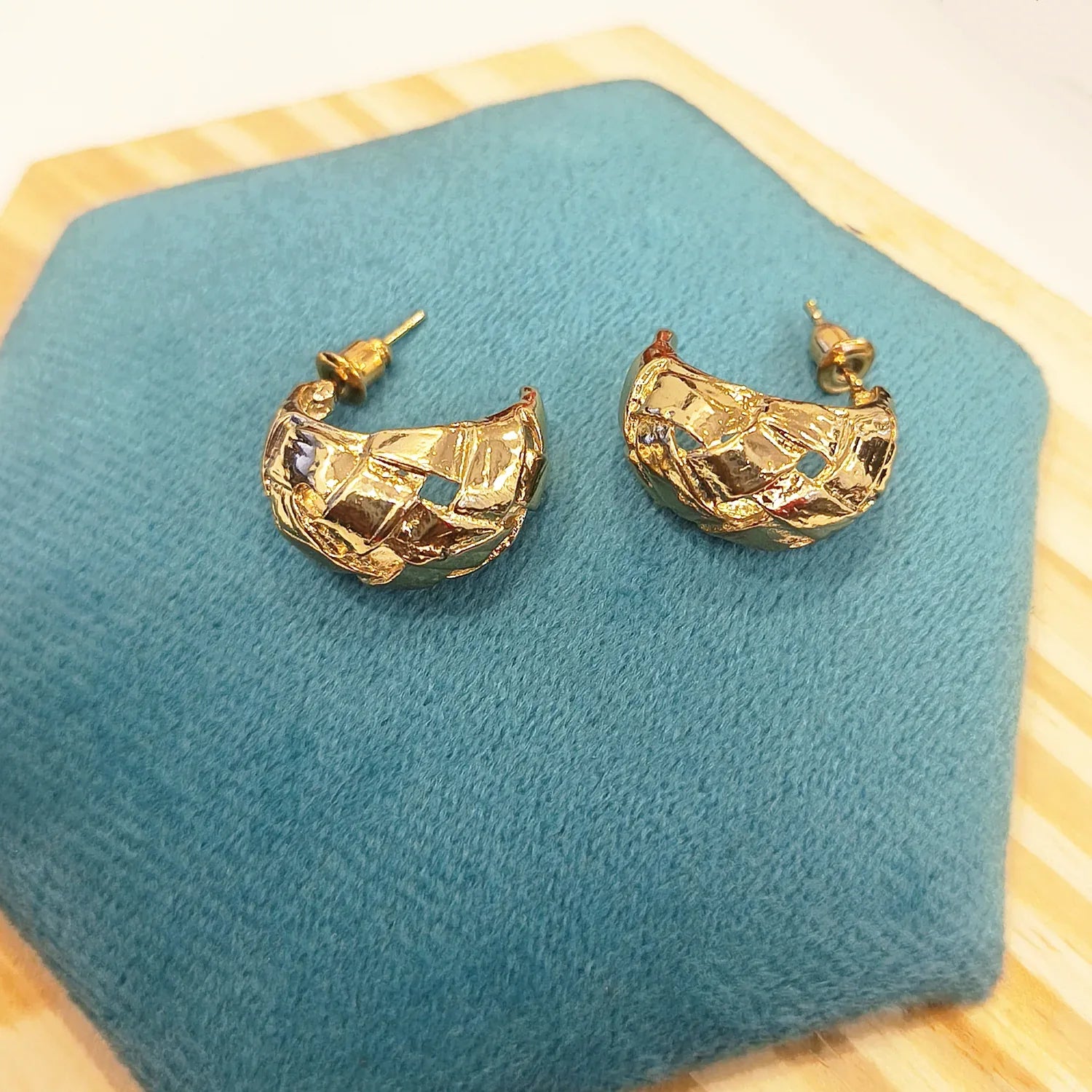 Gold hoop earrings on a blue cushion with a wooden base