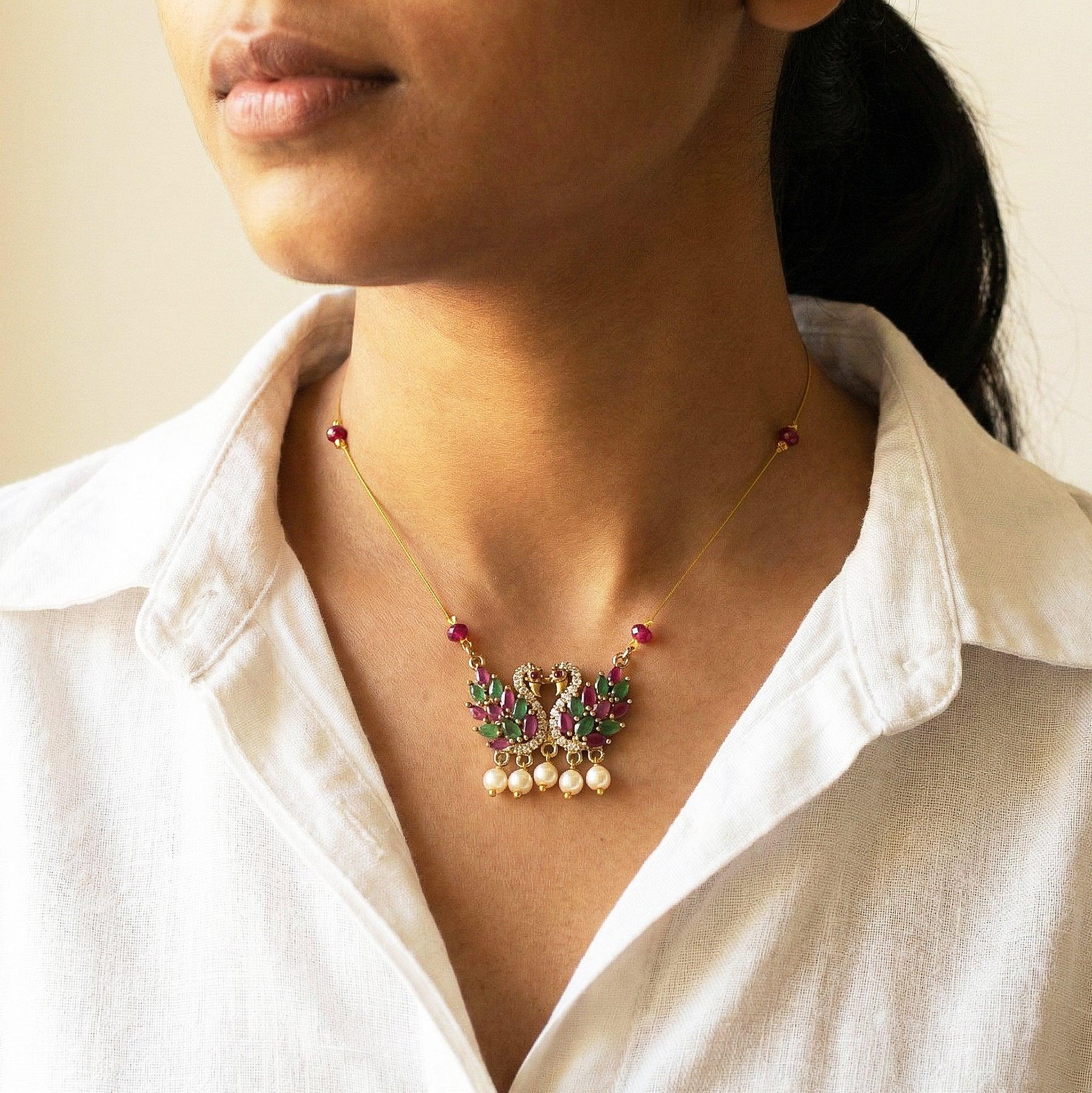 Woman wearing a delicate necklace with gemstones and pearls on a plain background